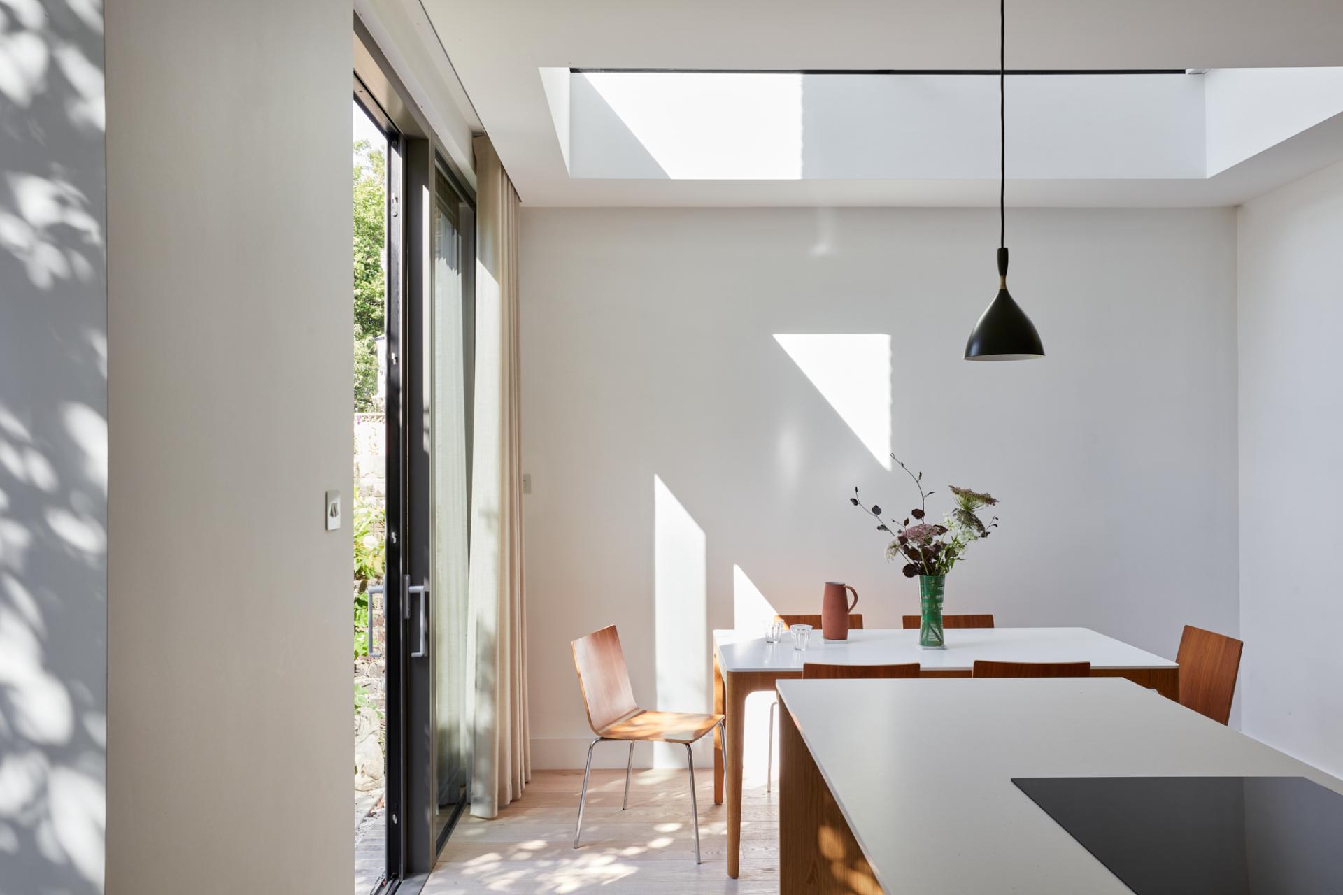 Bright, modern dining area featuring natural light, wooden furniture, and a vase of flowers, showcasing Woodsome Road's design aesthetic.