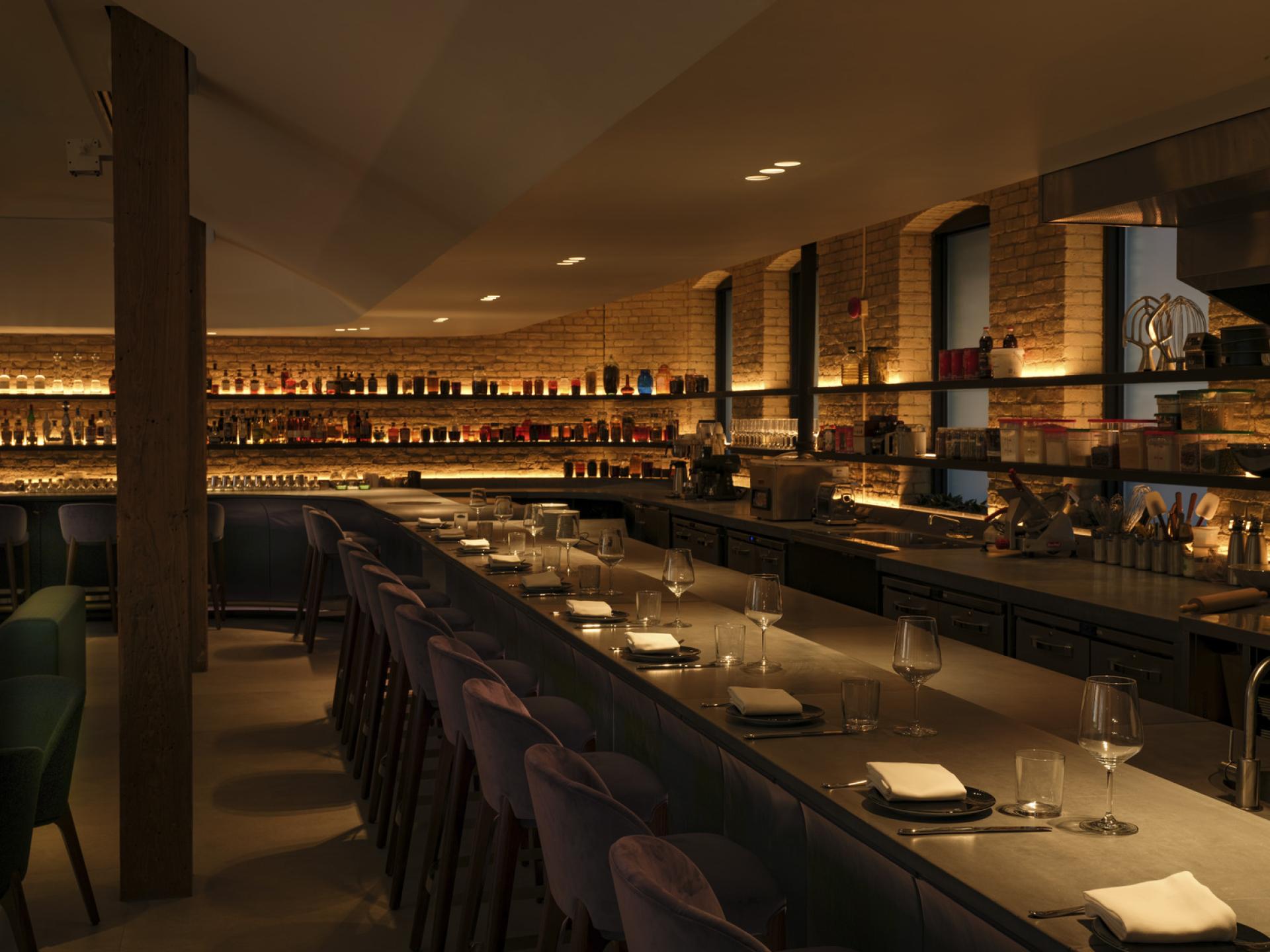 Stylish interior of VELA restaurant featuring a bar with illuminated shelves and elegant table settings.