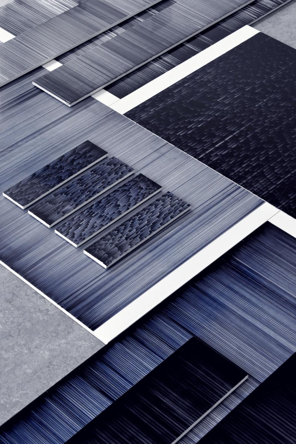 Dynamic patterned tiles in varying shades of blue and gray demonstrate Léa Mazy's innovative printing process for the tile industry.