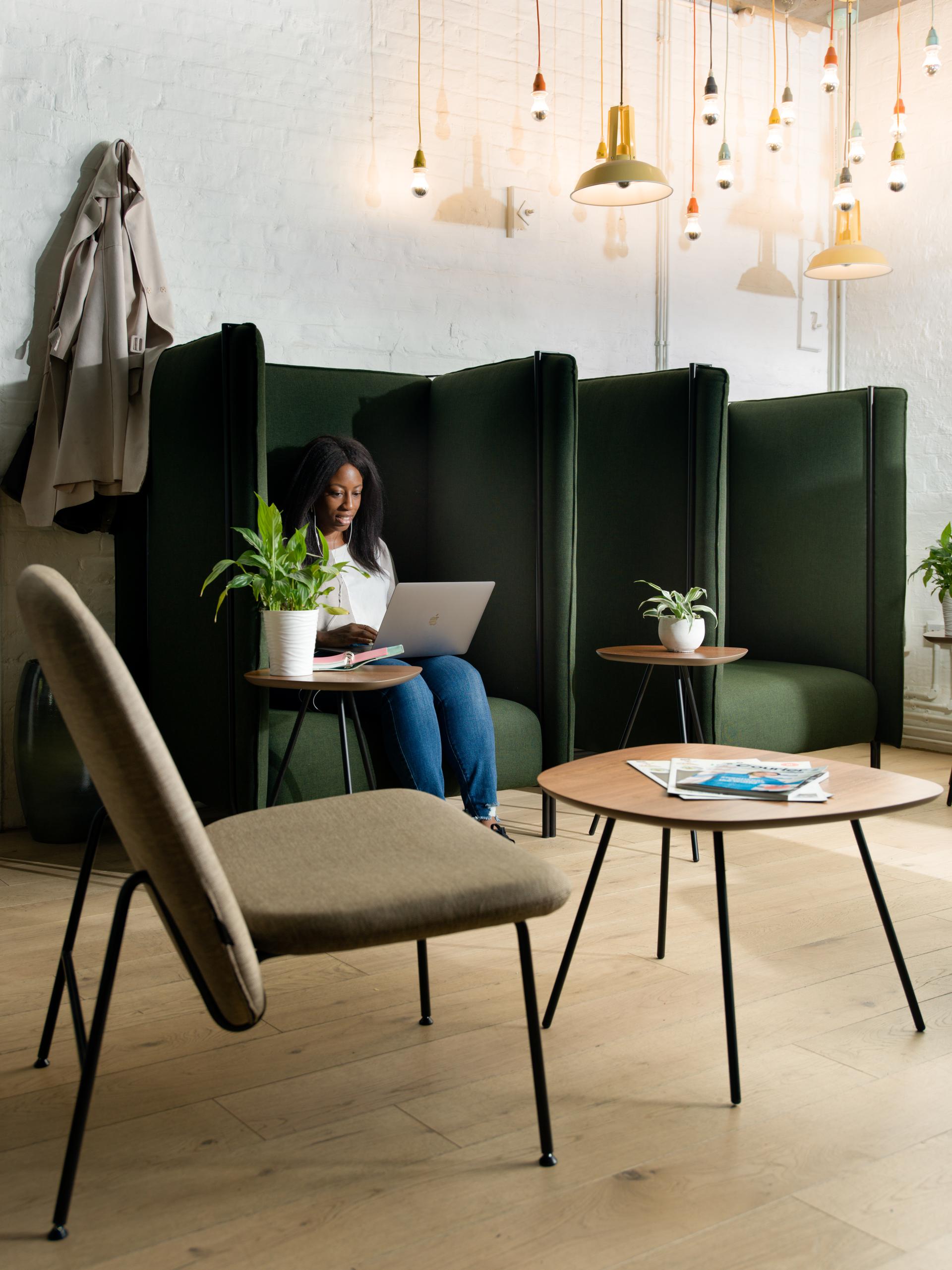 Contemporary workplace featuring a woman using a laptop in a cozy booth, surrounded by plants and stylish lighting.