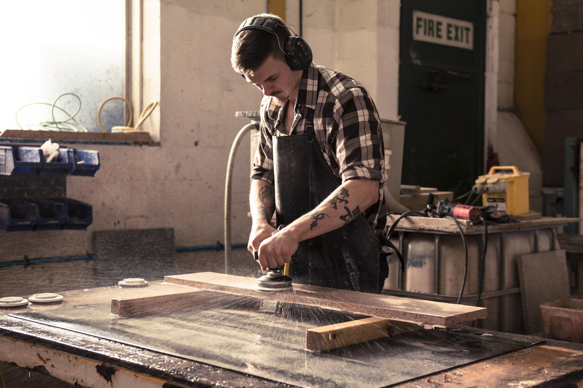 Craftsman using a power sander on a wooden surface in a workshop, highlighting sustainable material production.