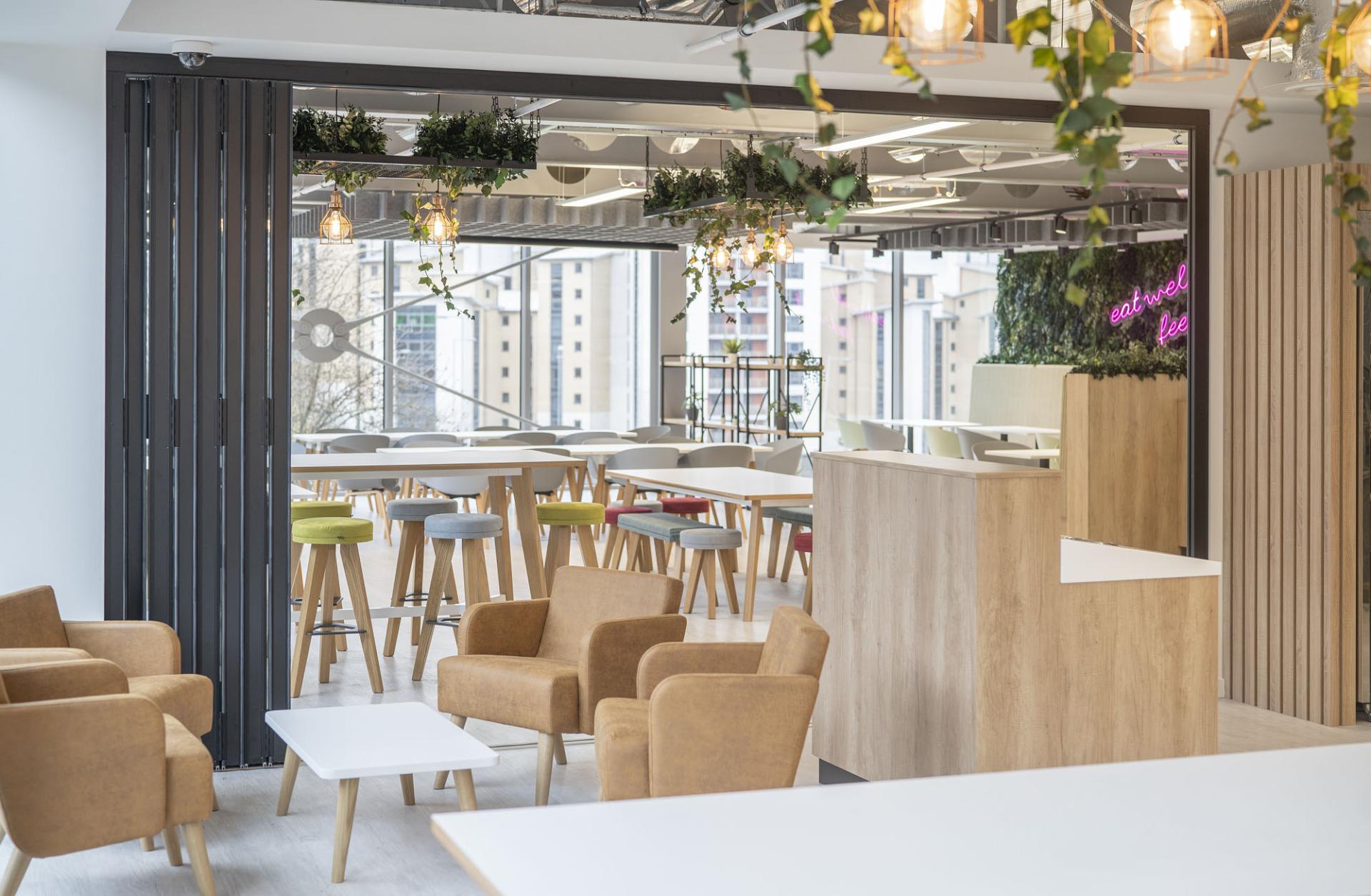 Contemporary office break area featuring flexible furniture, seating, and greenery, supporting employee creativity and comfort.