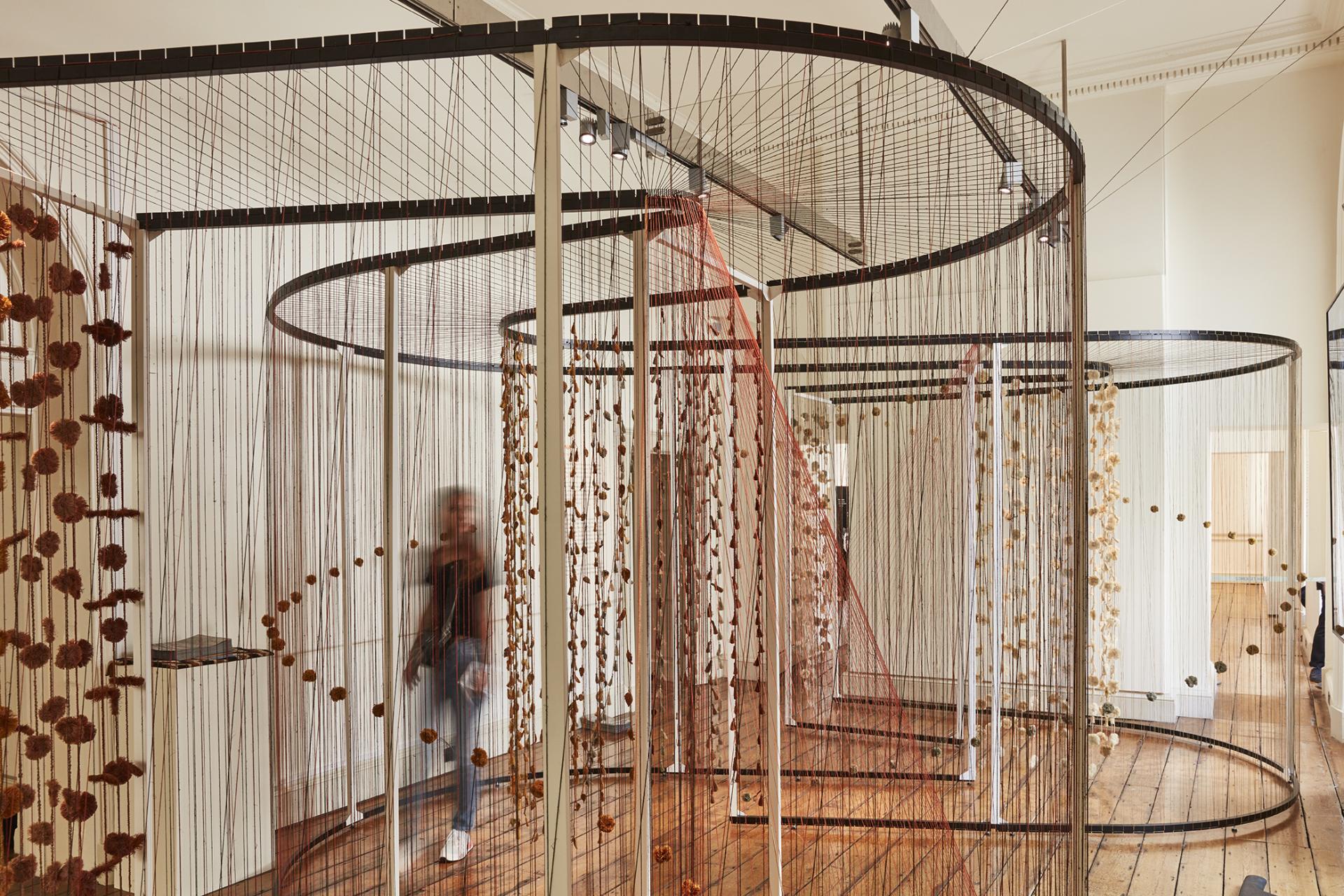 Creative installation at the London Design Biennale, featuring intricate hanging designs and a visitor exploring the space.