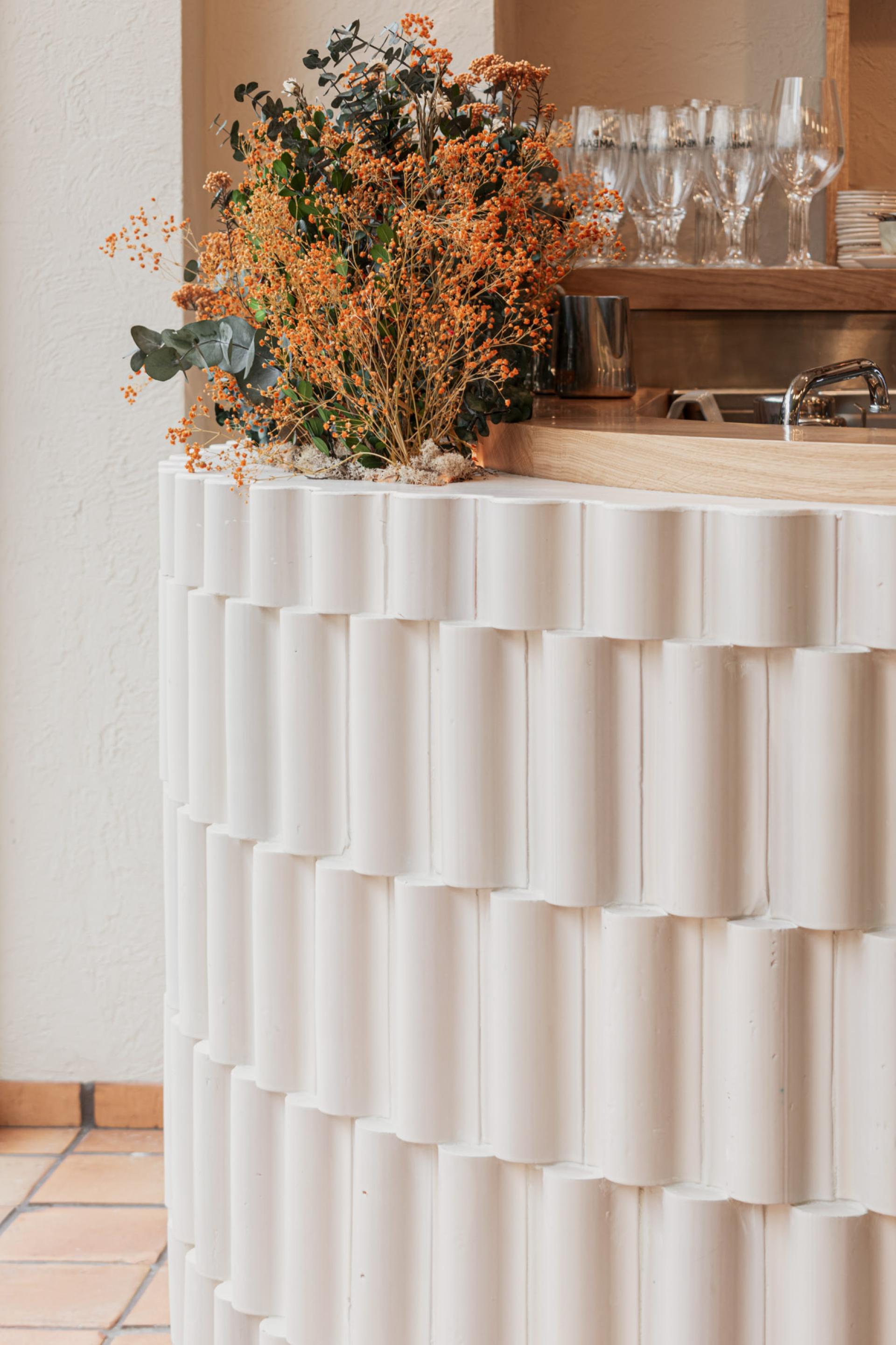 Floral arrangement with orange and green plants atop a textured white counter in a contemporary dining space.