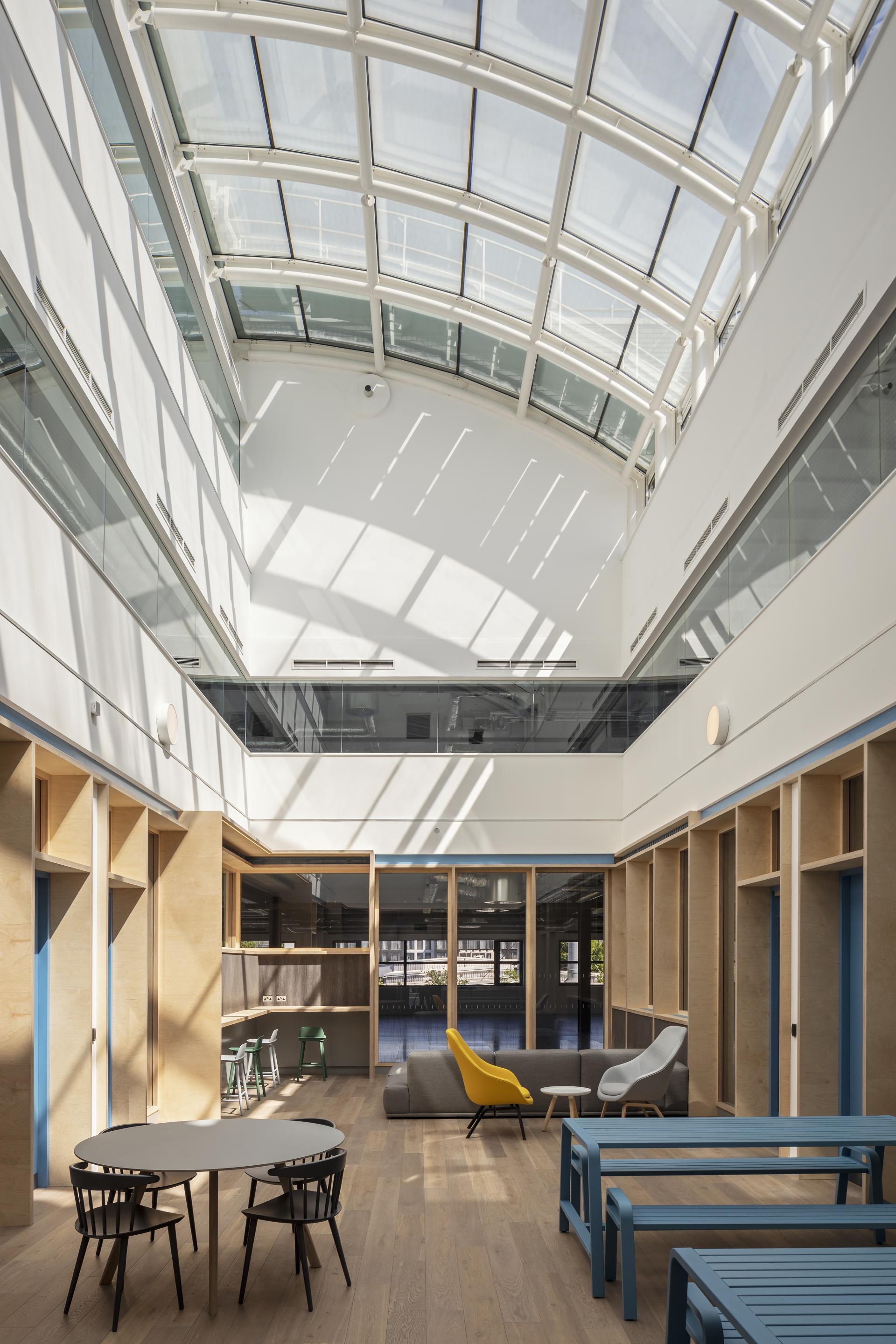 Bright, airy interior of 272GA office building featuring modern furniture, large skylights, and a wooden floor design.