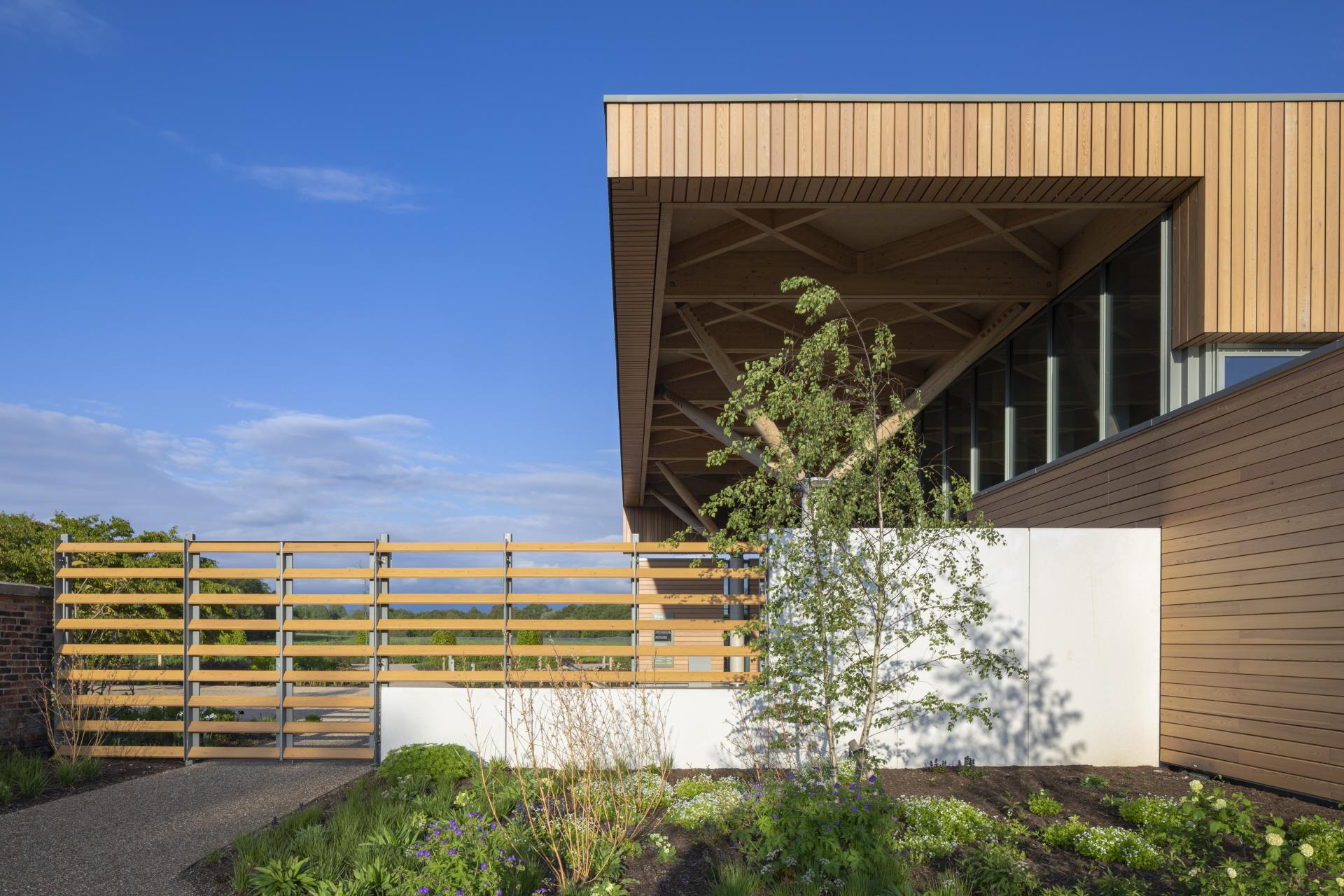 Modern architectural entryway at RHS Bridgewater featuring wooden accents, gardens, and a serene blue sky backdrop.