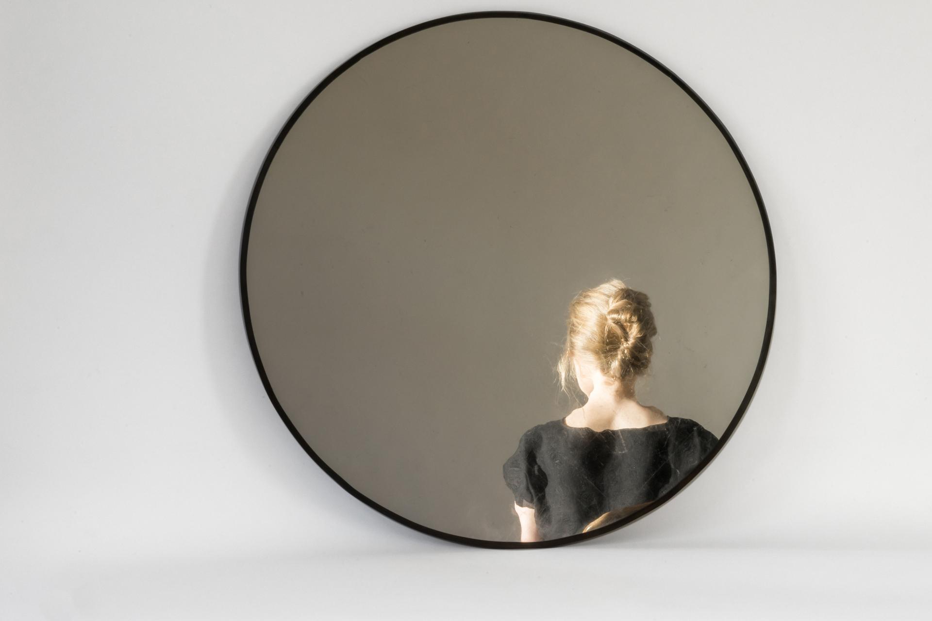 Reflection of a woman with braided hair in a circular mirror, showcasing the intersection of art and personal identity in Glasgow.