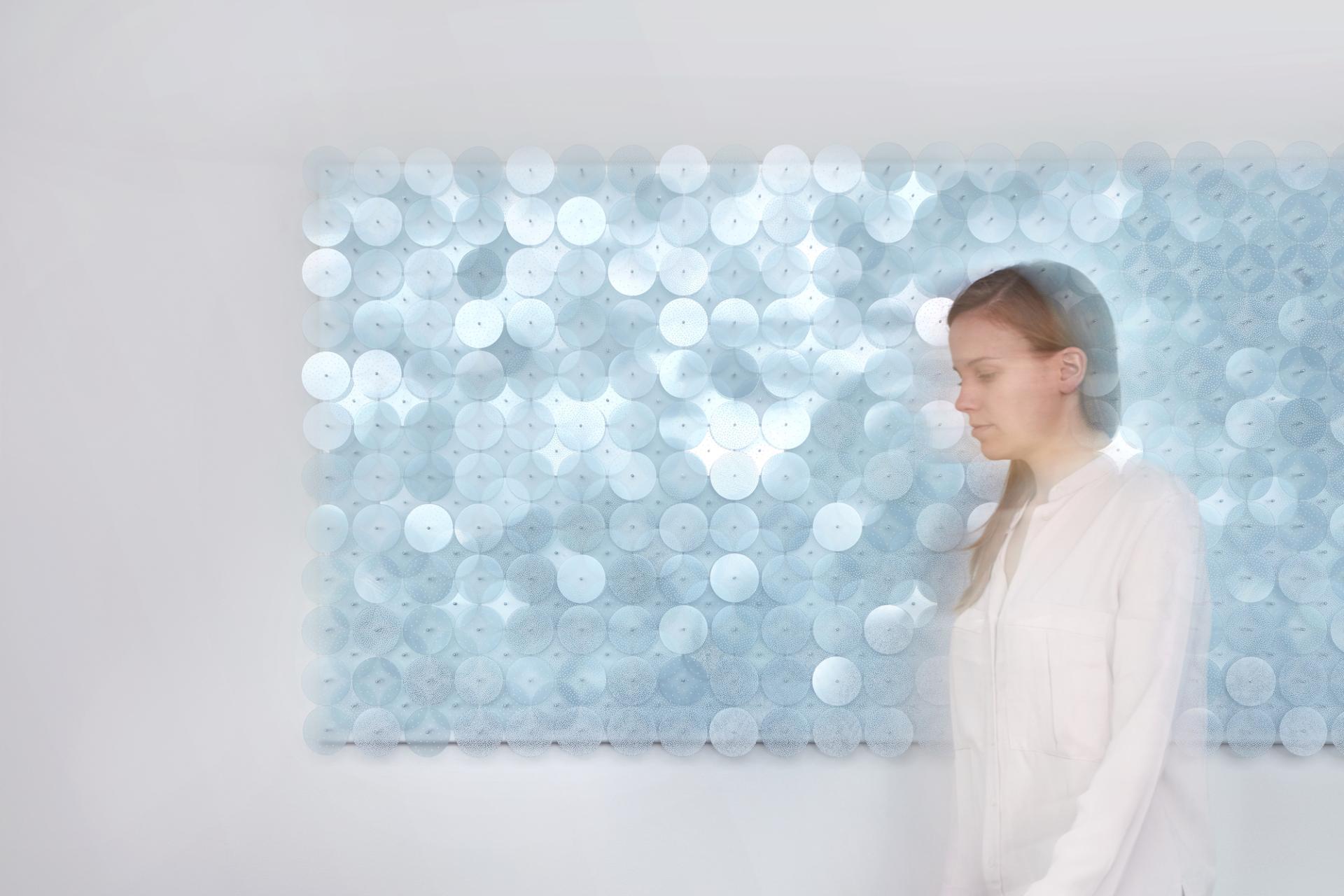 A visitor experiences tranquility by an art installation of layered blue and white discs, embodying sensory serenity.