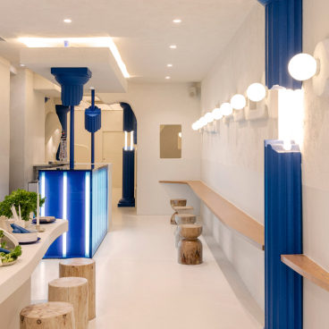 Contemporary Greek fast food interior design featuring blue columns, wooden seating, and a minimalist aesthetic at Egeo restaurant.