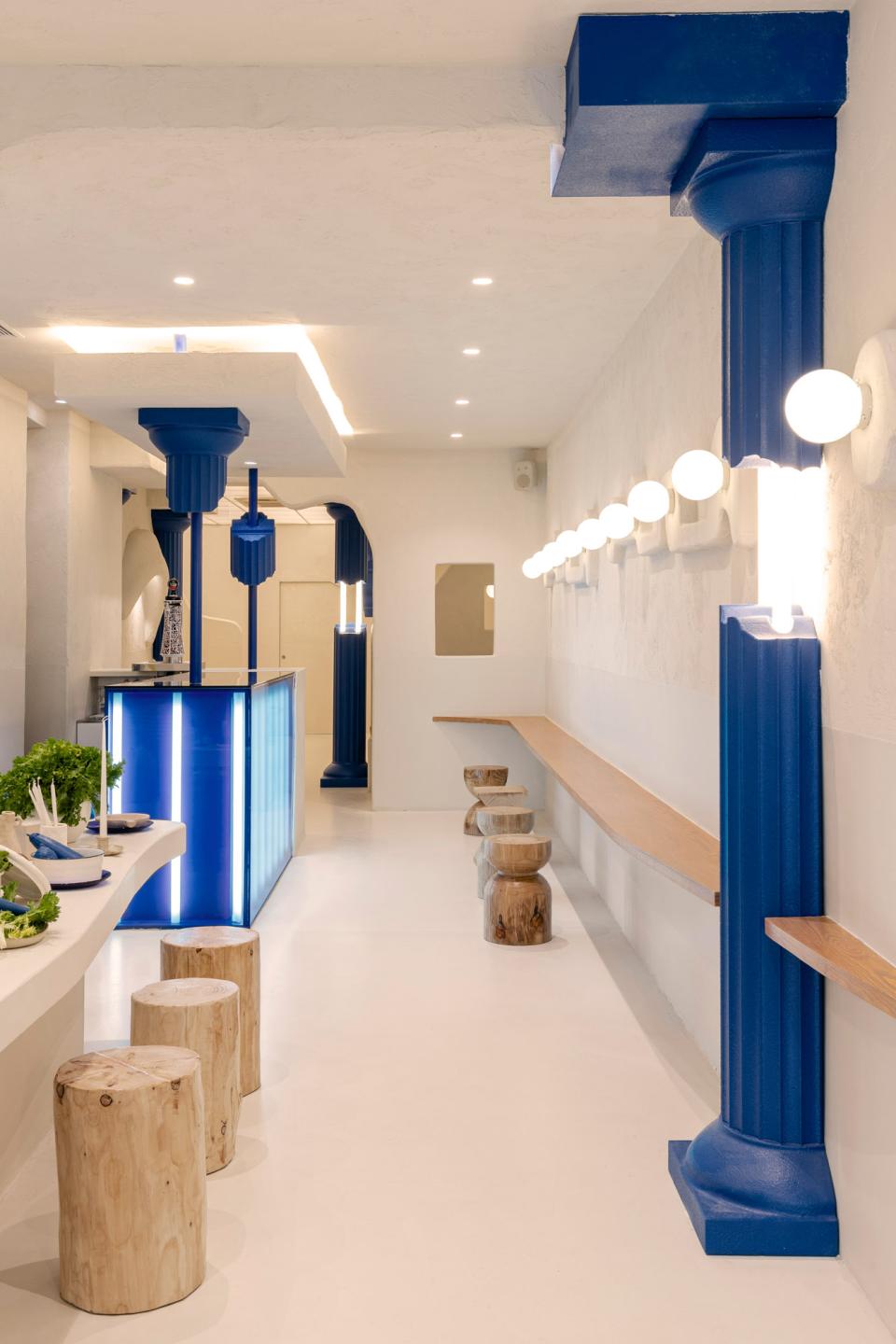Contemporary Greek fast food interior design featuring blue columns, wooden seating, and a minimalist aesthetic at Egeo restaurant.