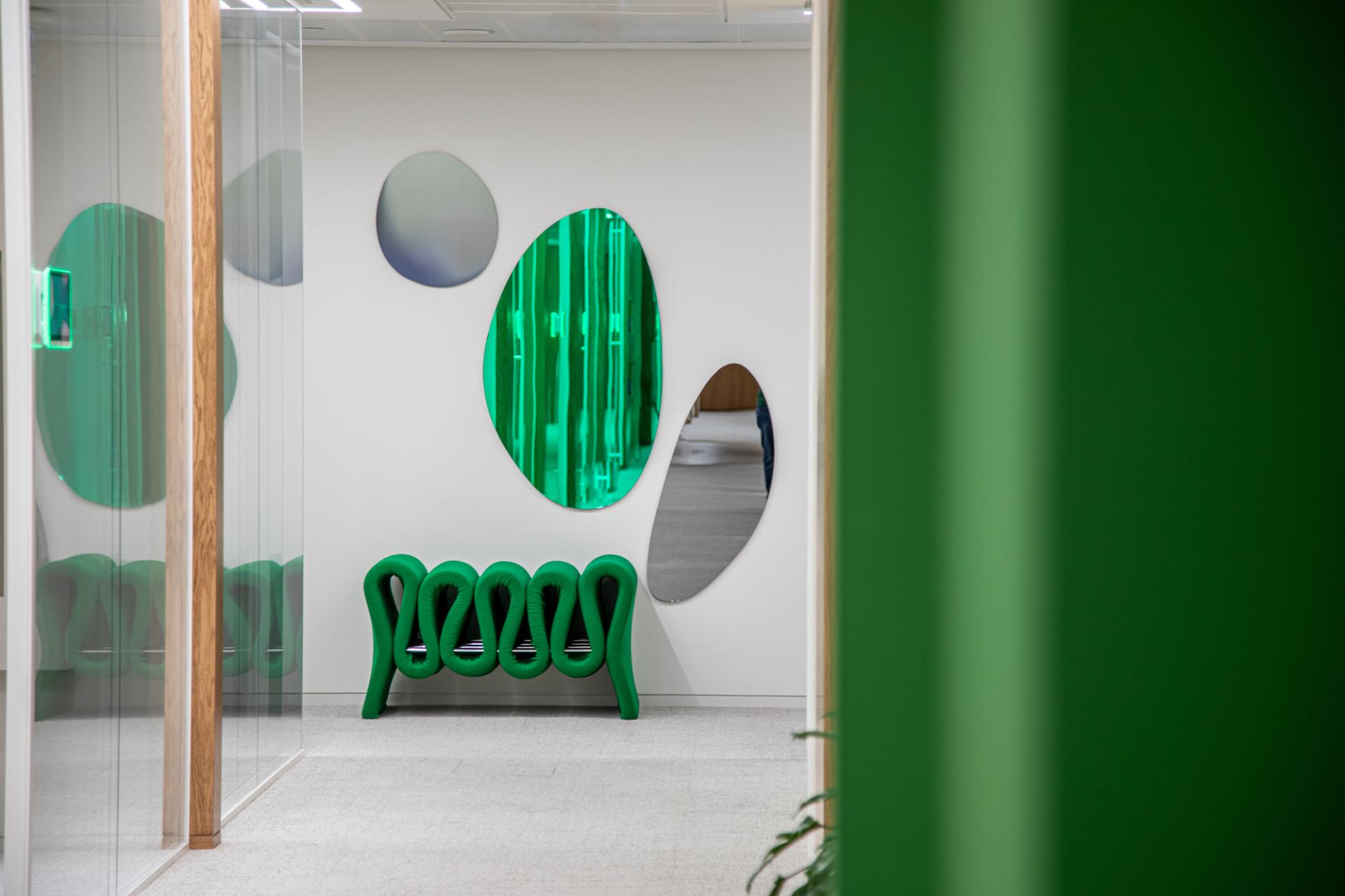 Vibrant green seating and reflective wall decor in a modern Dubai workplace inspired by nature.