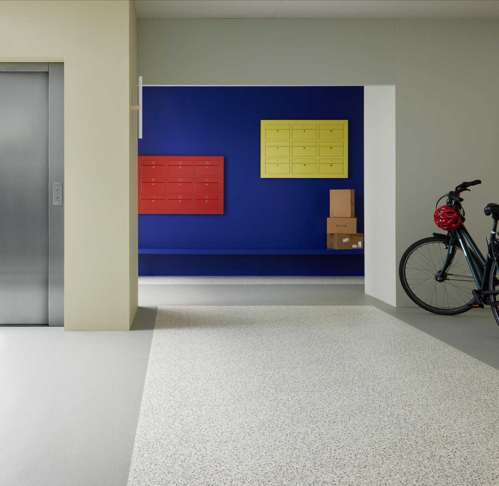 Modern interior featuring Forbo's Modul’up flooring, vibrant mailboxes, and a bicycle, illustrating contemporary design and refurbishment solutions.