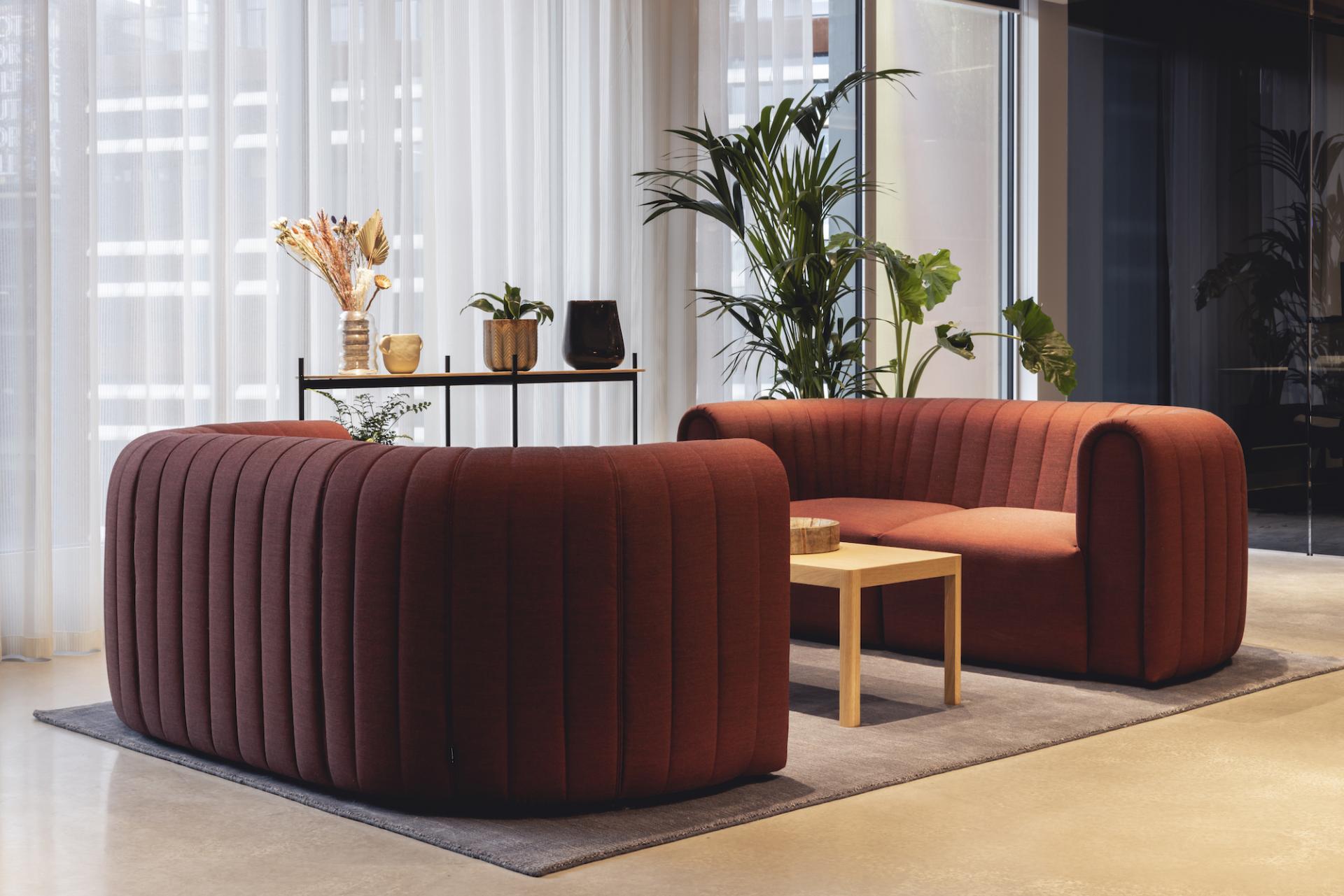 Modern workspace lounge with stylish red sofas, wooden table, and decorative plants, designed for AstraZeneca UK by Ekho Studio.