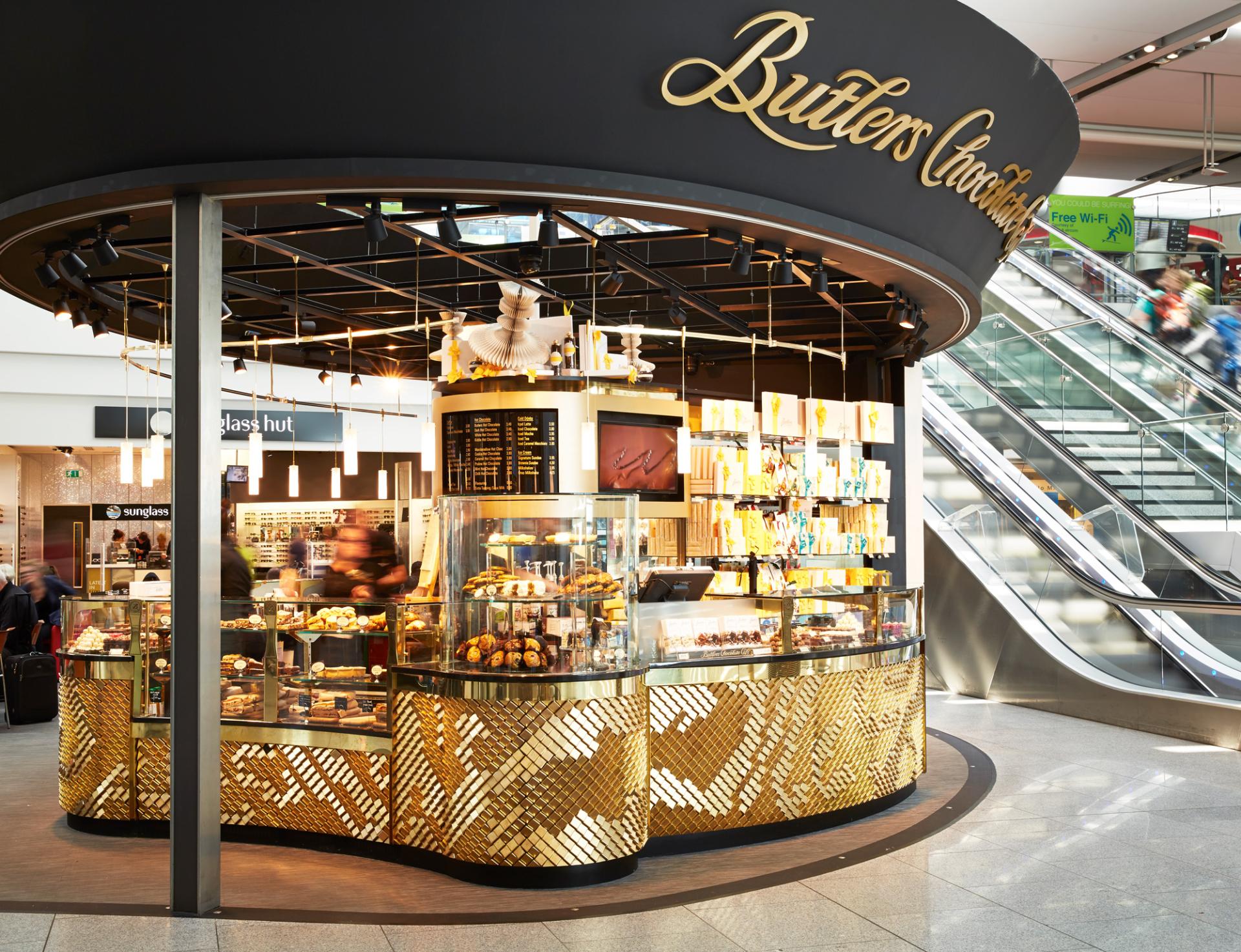 Chic chocolate shop design featuring golden accents and vibrant displays in a bustling airport setting.