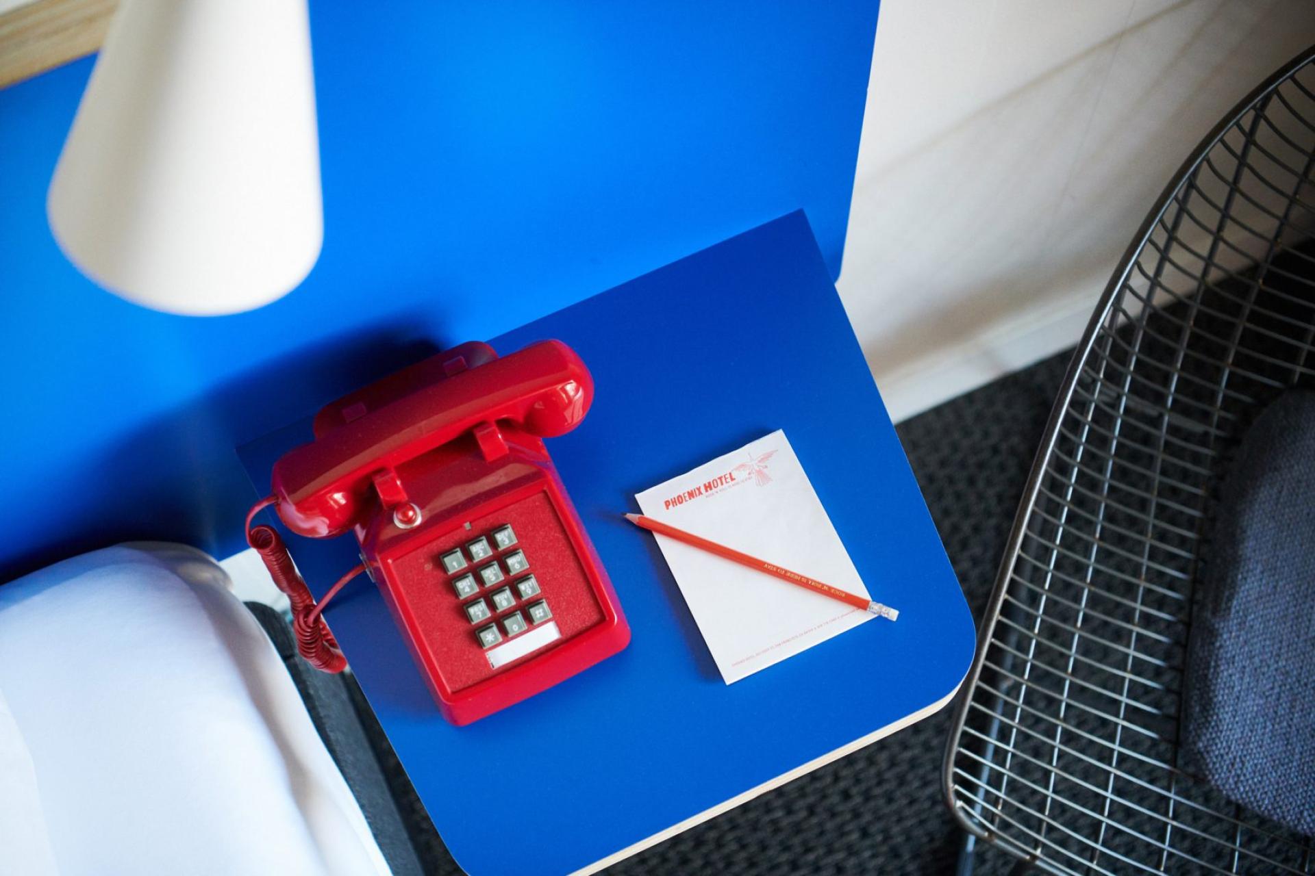 Bright red retro telephone next to notepad and pencil on blue table in Phoenix Hotel, San Francisco.