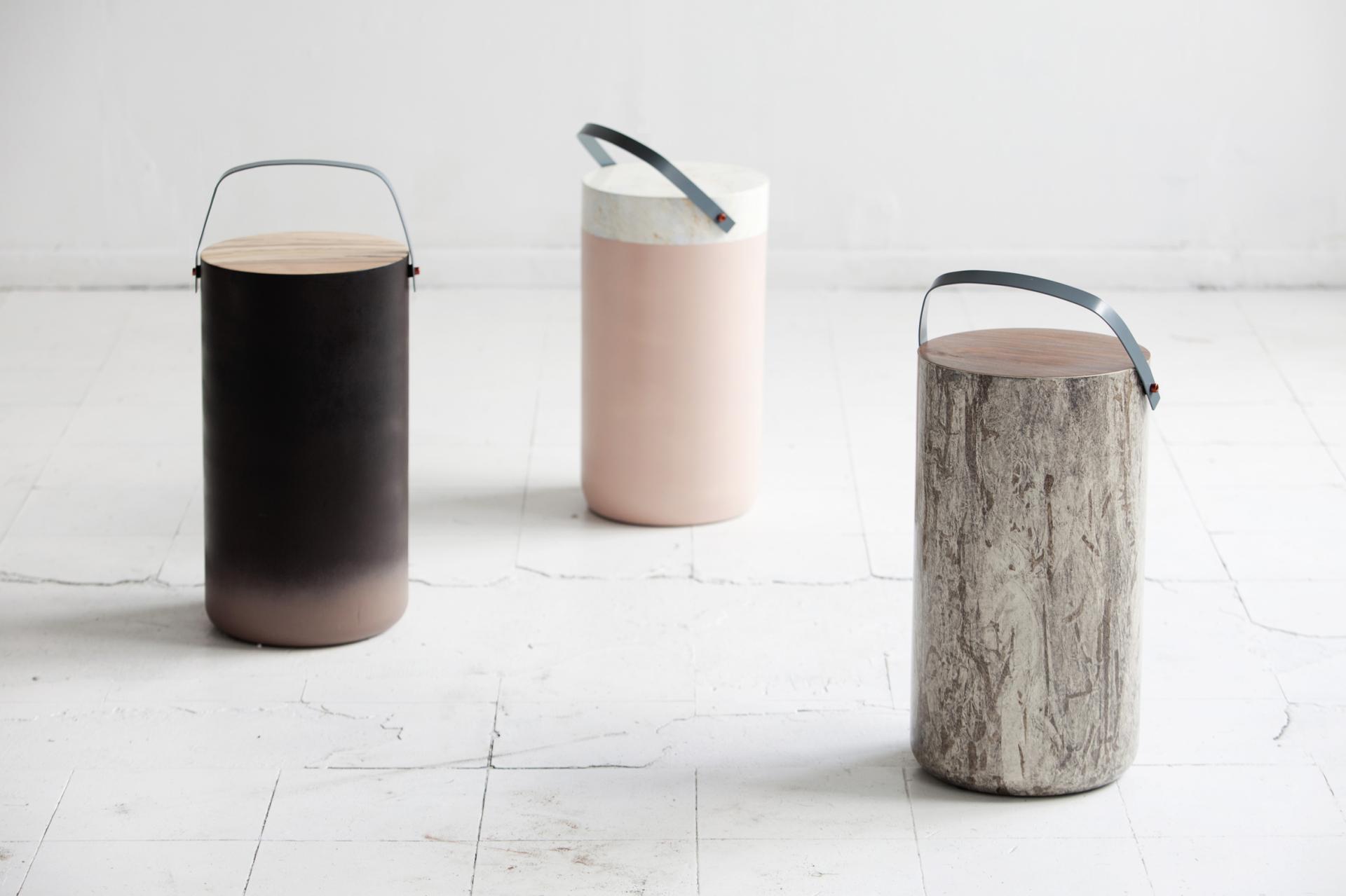 Three experimental cylindrical stools in varying textures and colors displayed in a minimalist gallery setting.