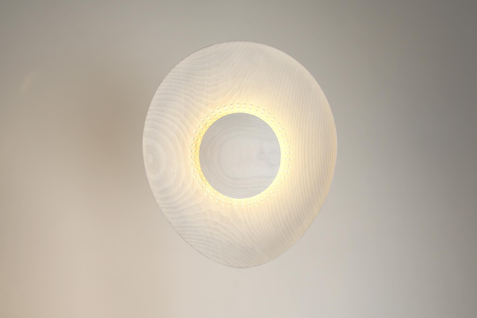 Sculptural wooden light fixture featuring a circular design and warm glow, showcased at New Designers 2024.