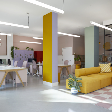 Brightly colored London office featuring collaborative desks, vibrant decor, and a cozy yellow sofa, reflecting Mustard Made's creative inspiration.