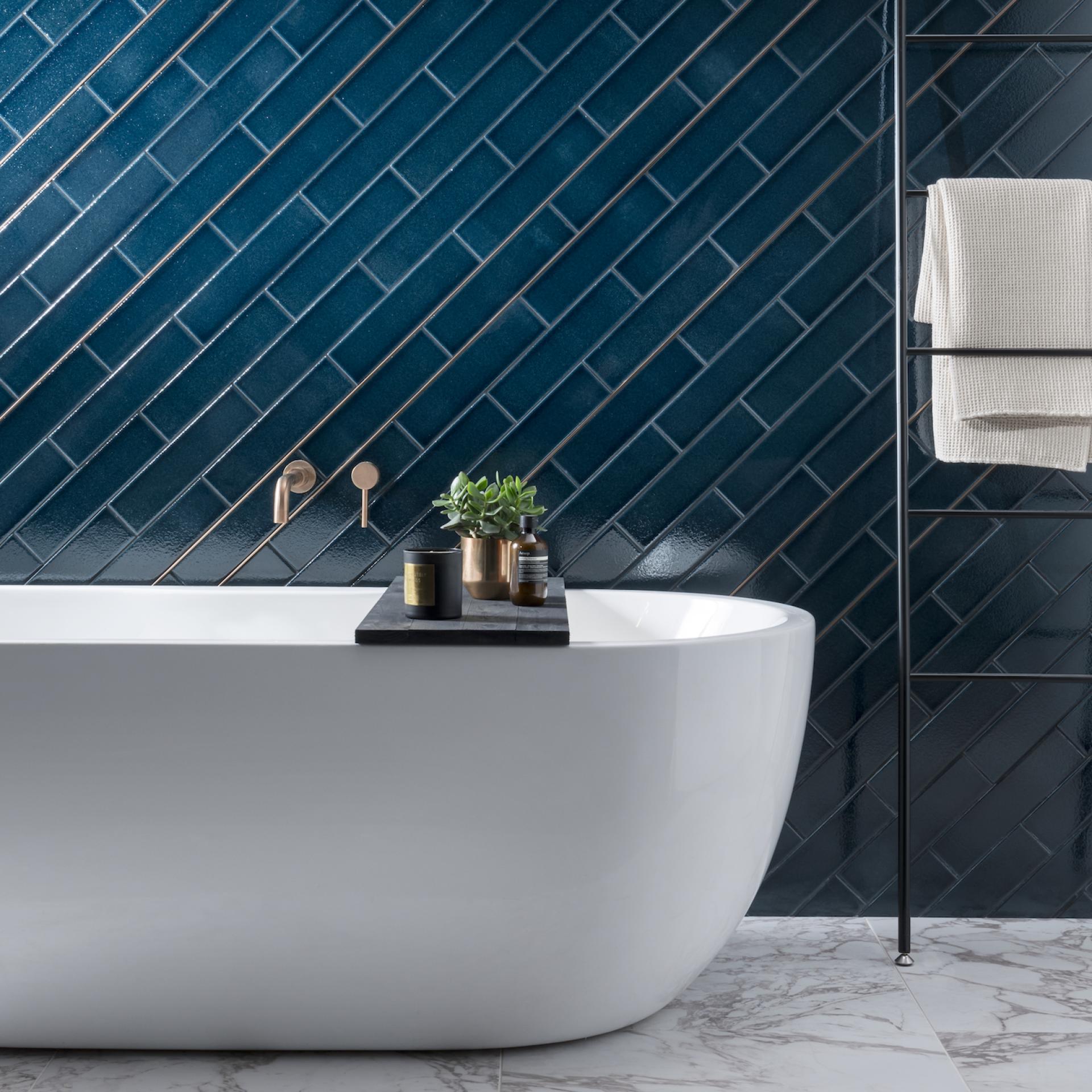 Elegant freestanding bathtub against a vibrant blue tiled wall, featuring modern accessories and a stylish decor setup.