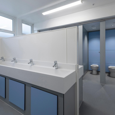 Modern gender-neutral washroom with sinks and toilet stalls, showcasing inclusive design in educational environments.