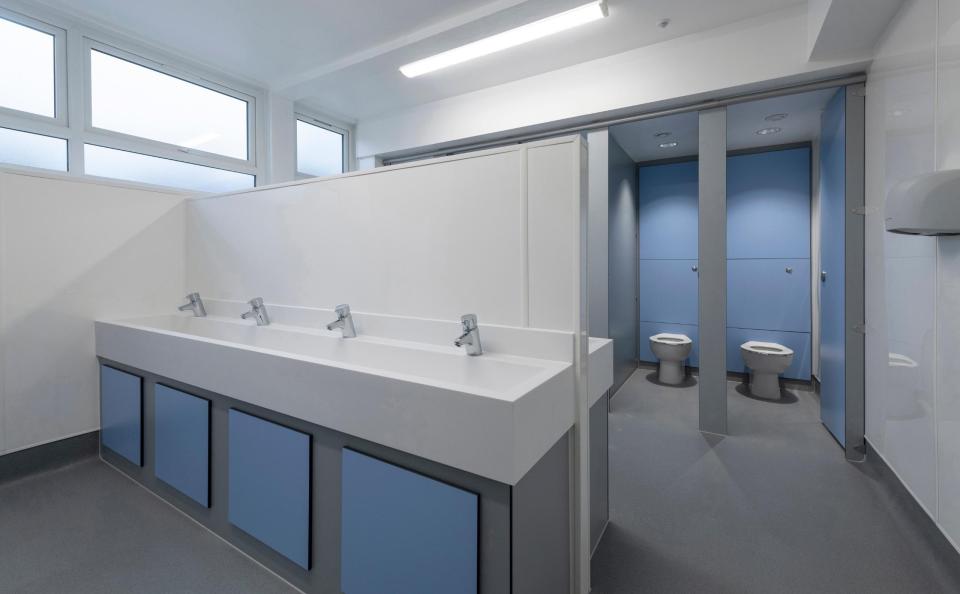 Modern gender-neutral washroom with sinks and toilet stalls, showcasing inclusive design in educational environments.