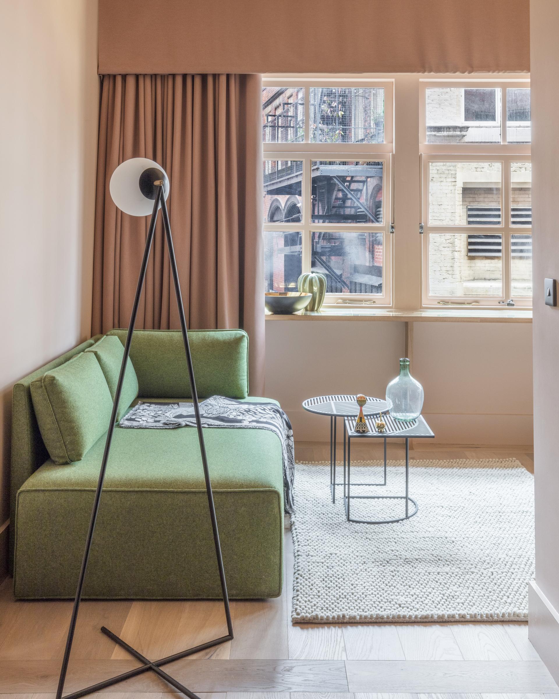 Stylish interior of Whitworth Locke aparthotel featuring a green sofa, decorative lamp, and natural light from large windows.