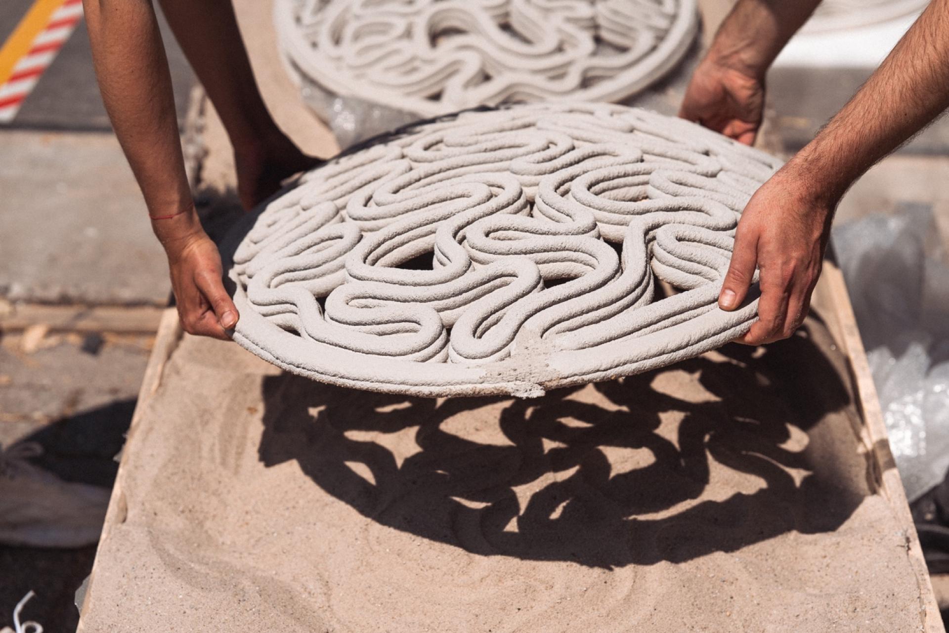 Hands holding a 3D printed concrete mold with intricate designs, showcasing innovative construction techniques in architecture.