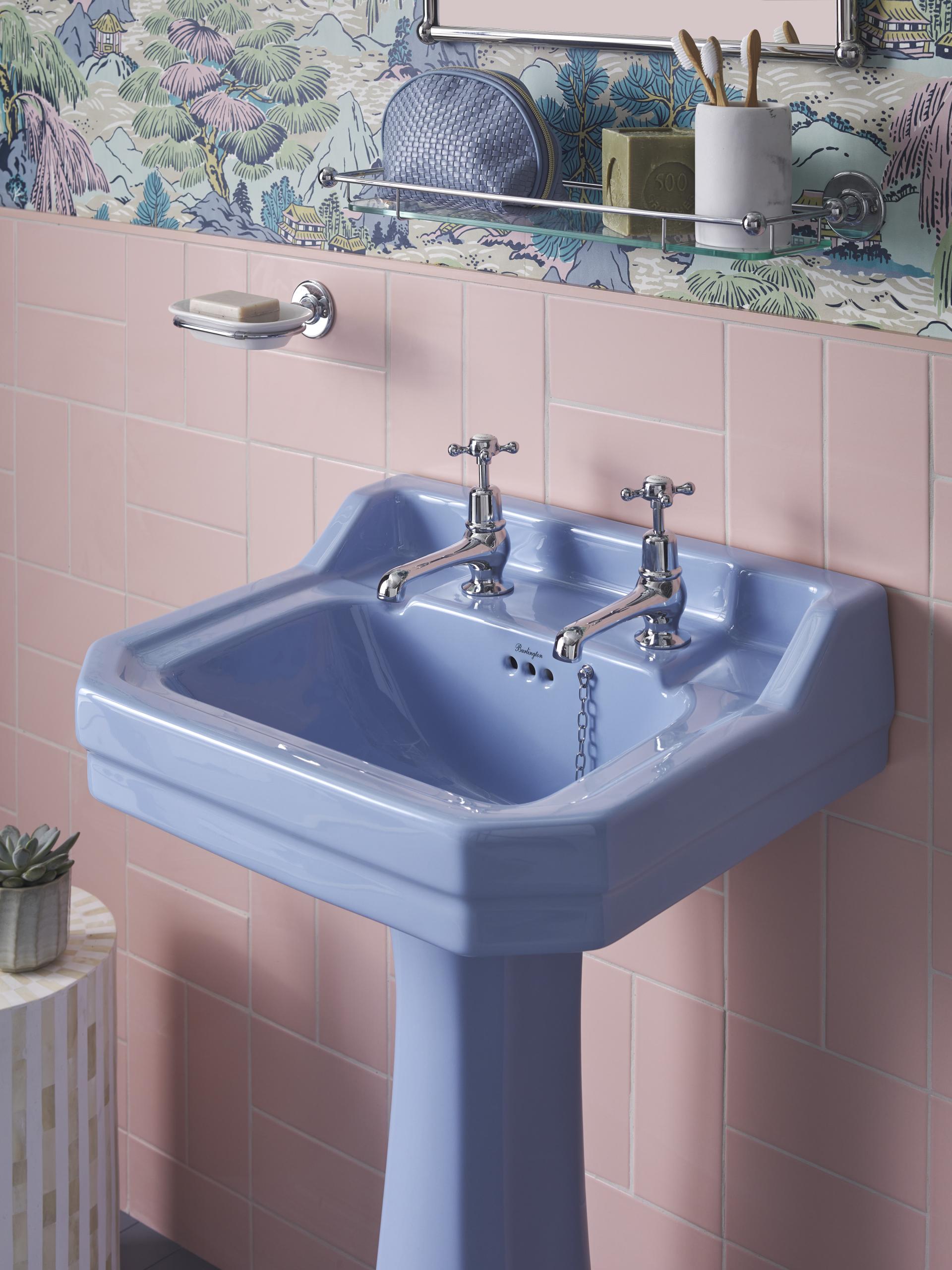 Stylish pastel blue sink with vintage faucets, surrounded by pink tiles and playful wallpaper for modern bathroom design inspiration.