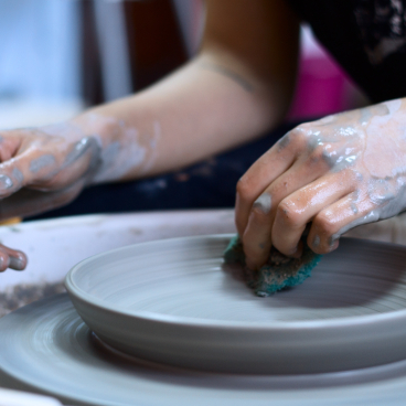 Hands shaping a ceramic plate on a pottery wheel, showcasing Manchester's vibrant craft scene.
