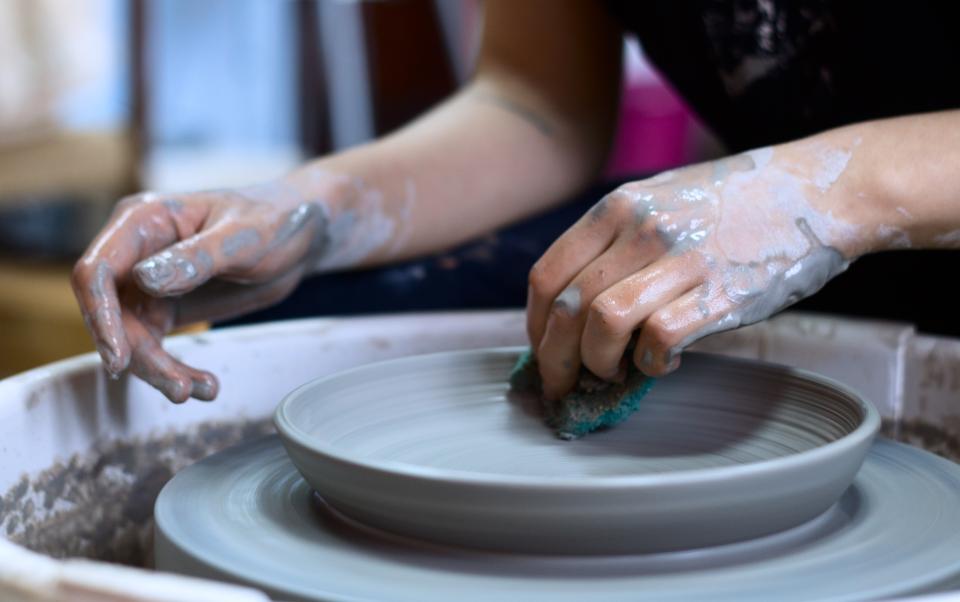 Hands shaping a ceramic plate on a pottery wheel, showcasing Manchester's vibrant craft scene.