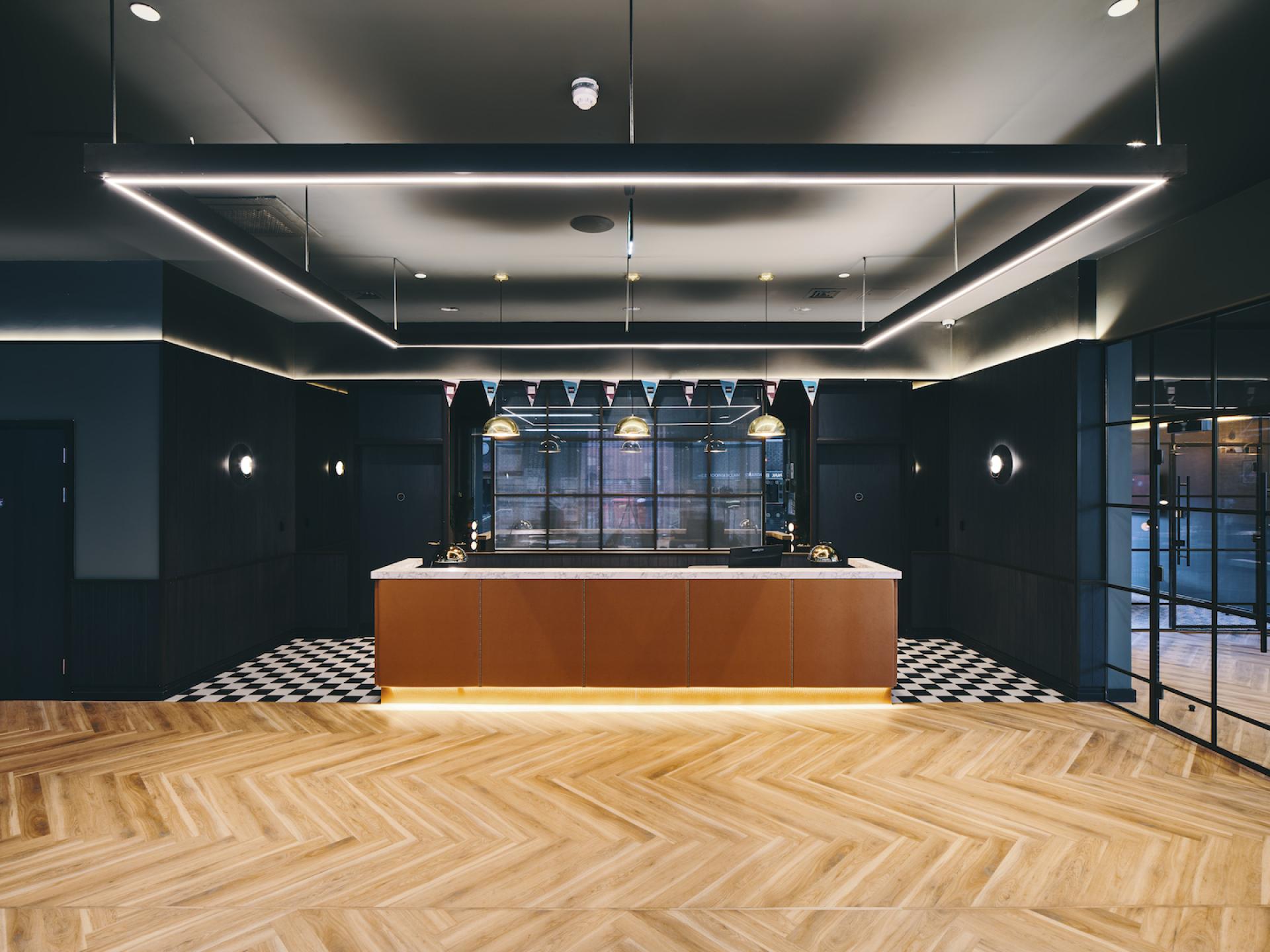 Sophisticated reception area of a modern student amenity space featuring elegant lighting and stylish wooden flooring.