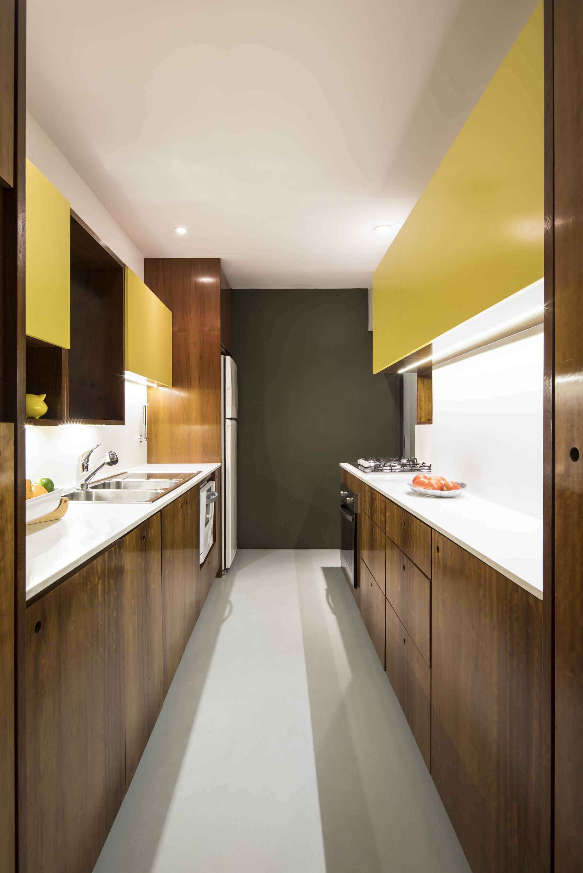 Renovated mid-century kitchen featuring wooden cabinets, yellow accents, and modern appliances in a São Paulo apartment.
