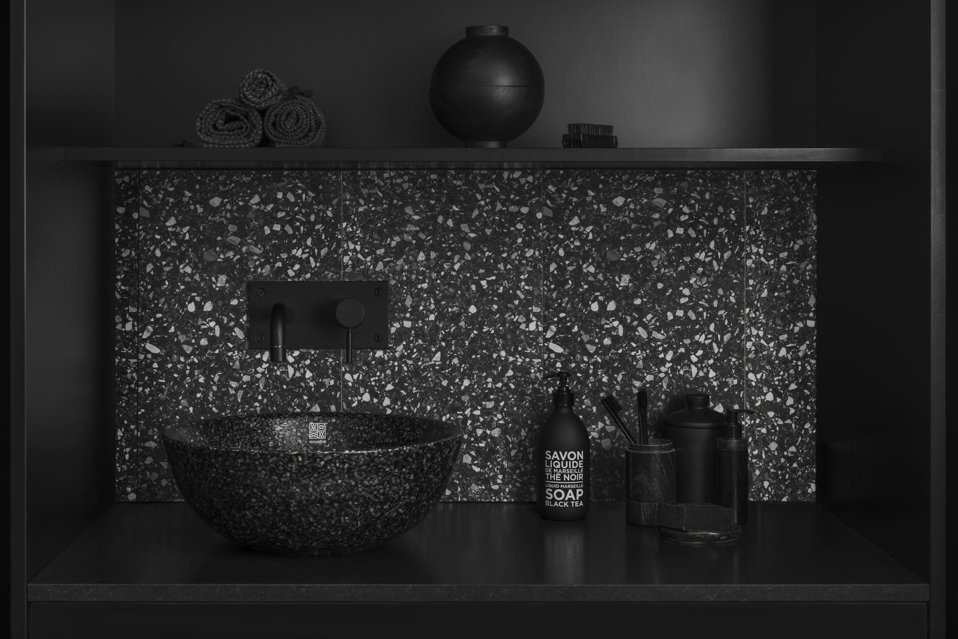 Stylish low-carbon washroom featuring a black composite sink, stylish soap dispenser, and decorative accessories on dark shelves.