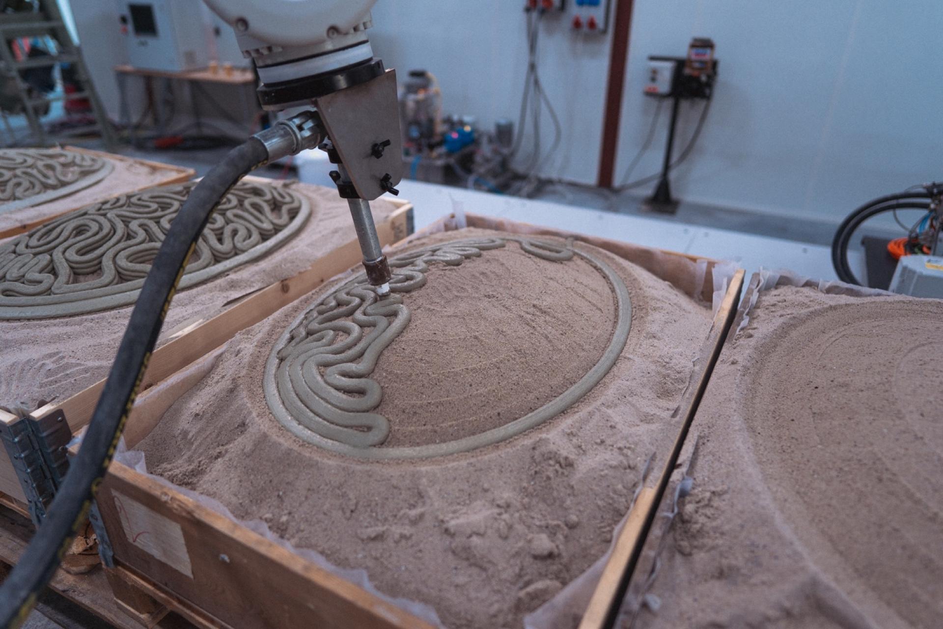 Robotic arm extruding a concrete-like material into sand molds, showcasing innovative 3D printing in construction.