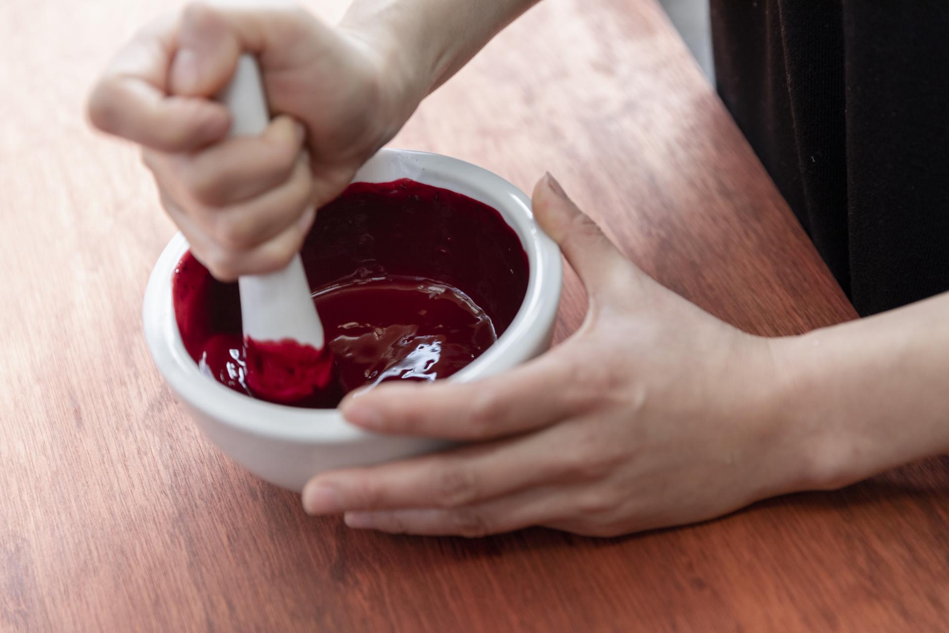 Hand using a pestle to mix vibrant red dye in a bowl, showcasing traditional Japanese dyeing techniques.