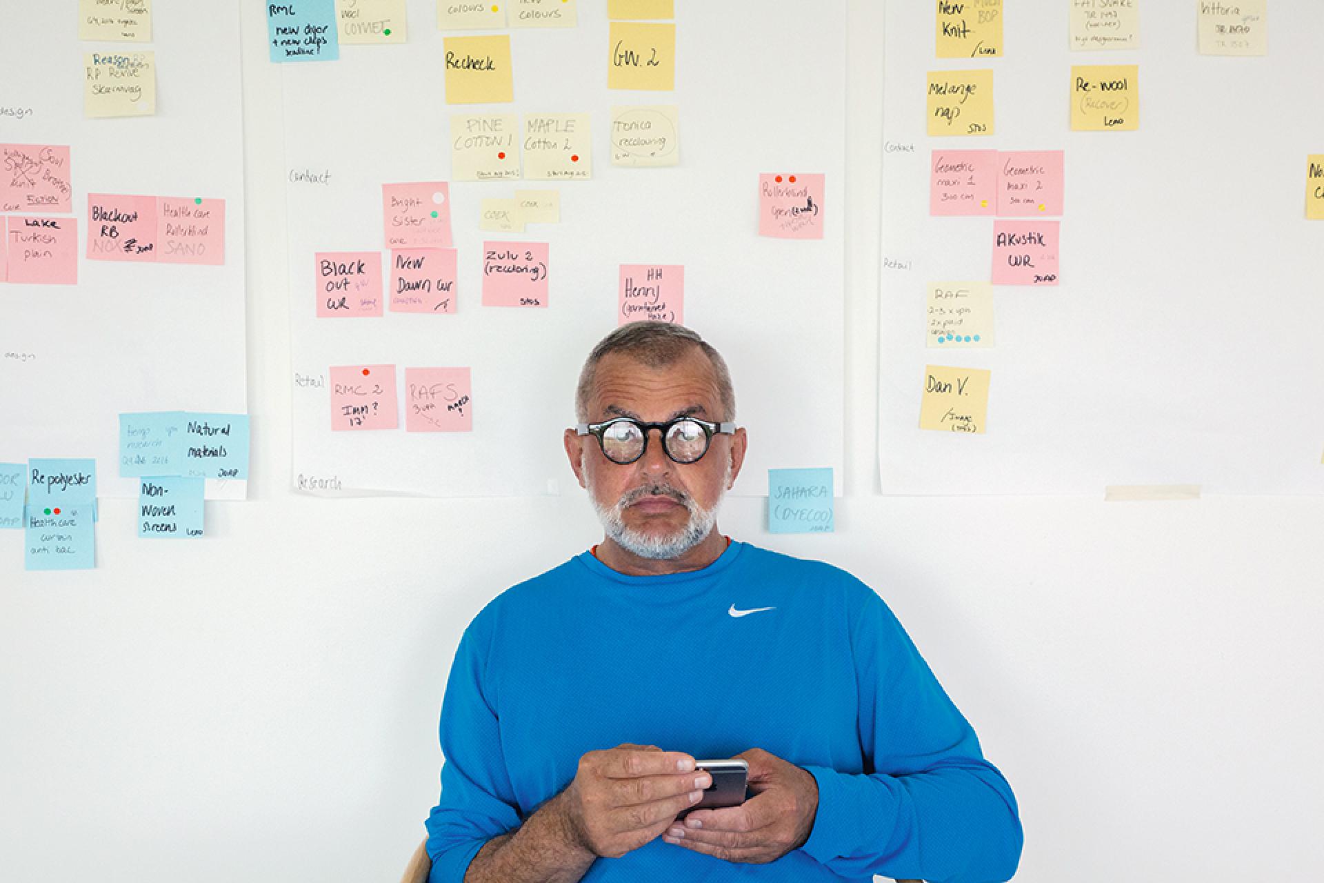 Giulio Ridolfo sitting in front of a wall filled with colorful notes, reflecting on textile color design and innovation.