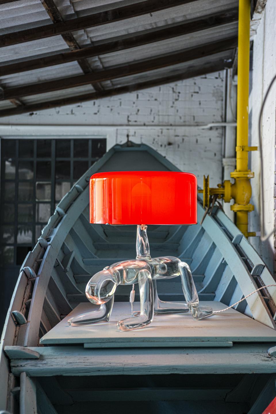 A unique glass lamp sculpture featuring a transparent figure, set against a blue wooden boat backdrop.