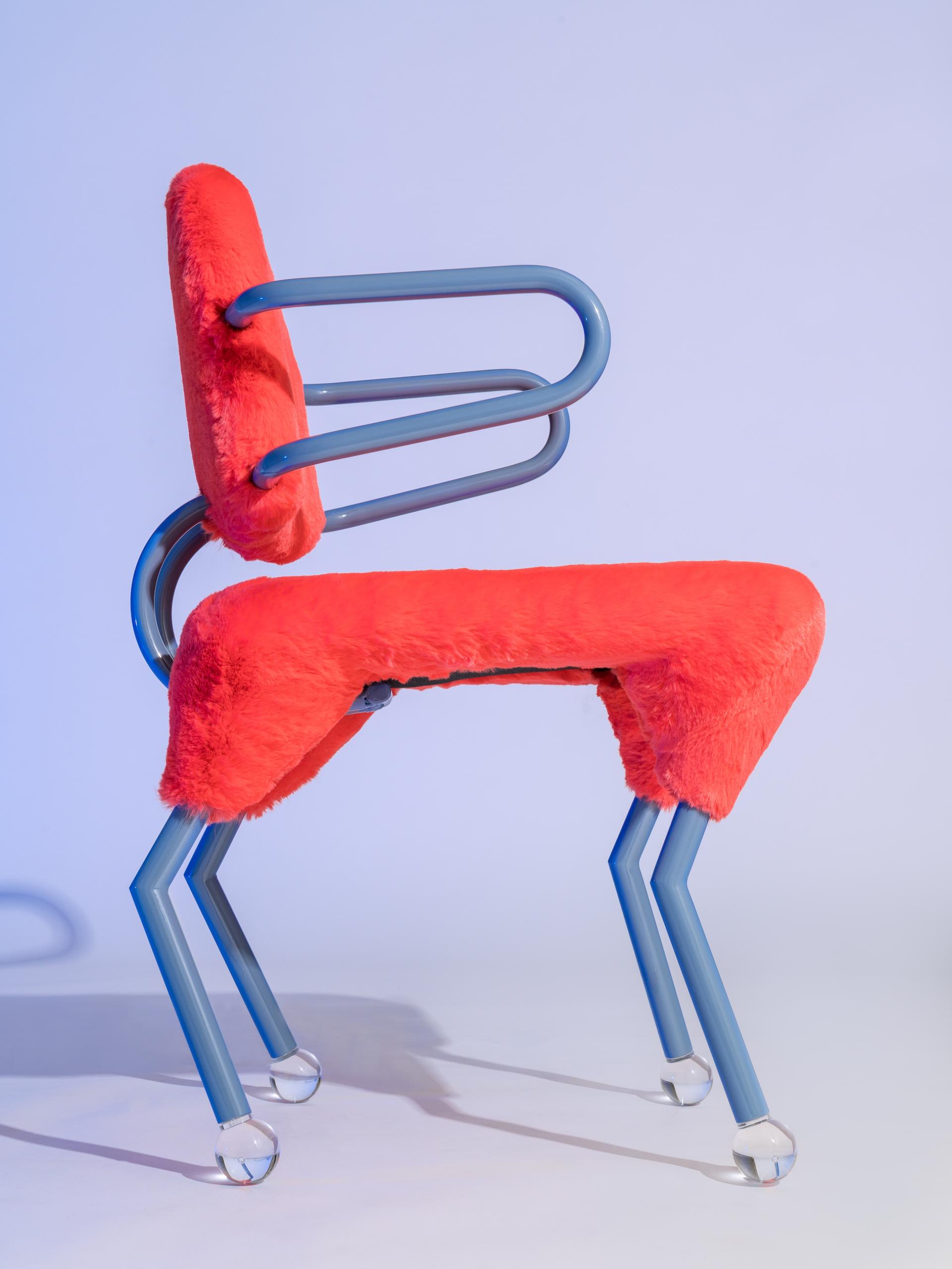 Vibrant red furry chair with blue metal frame, showcasing Memphis design aesthetic in a contemporary setting.