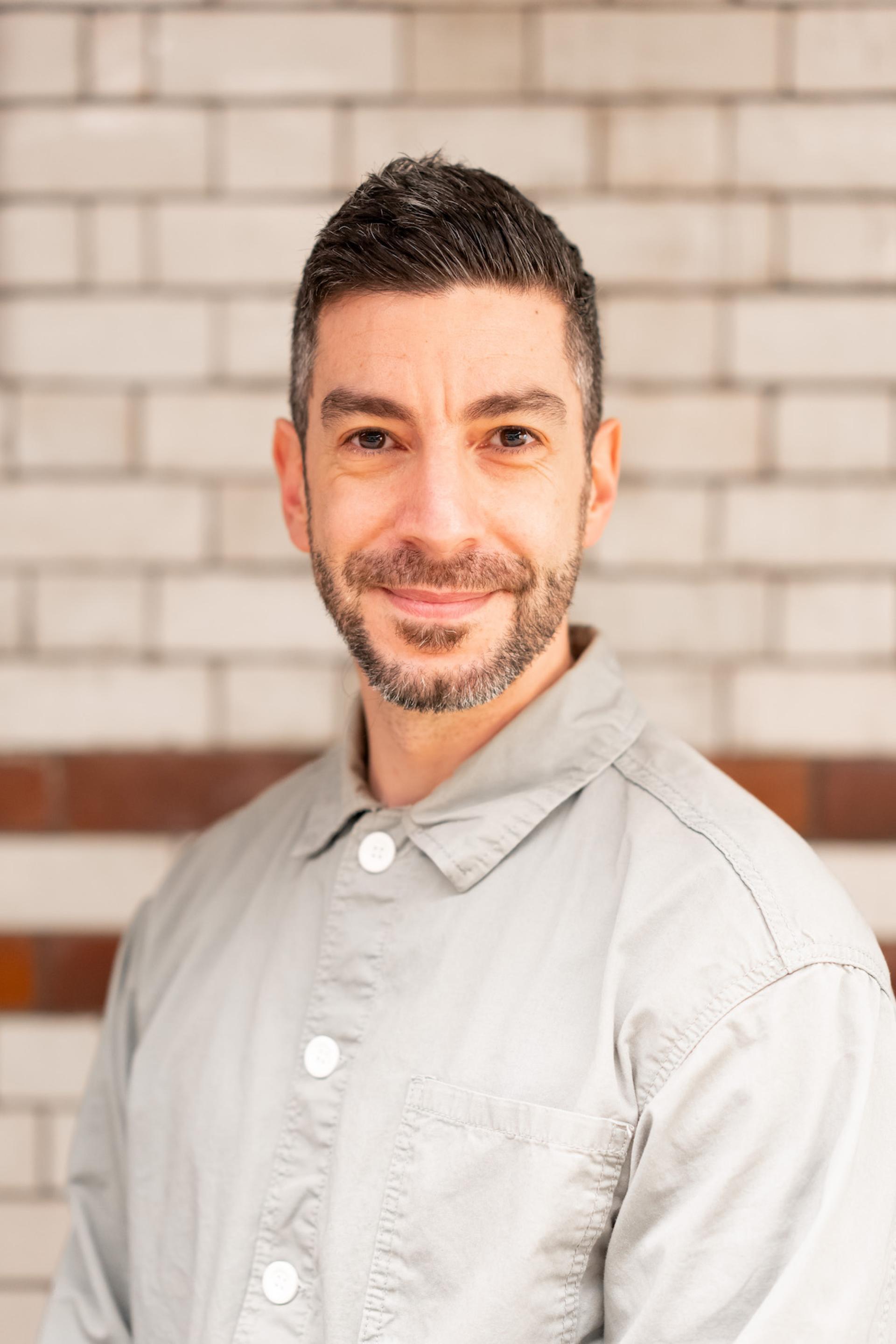 Professional man smiling in gray shirt, discussing sustainability and value engineering strategies in a modern environment.