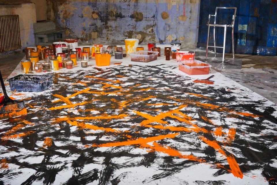 Colorful paint splatters on a floor with various paint containers, showcasing the artistic process behind Forbo's Starck flooring collection.