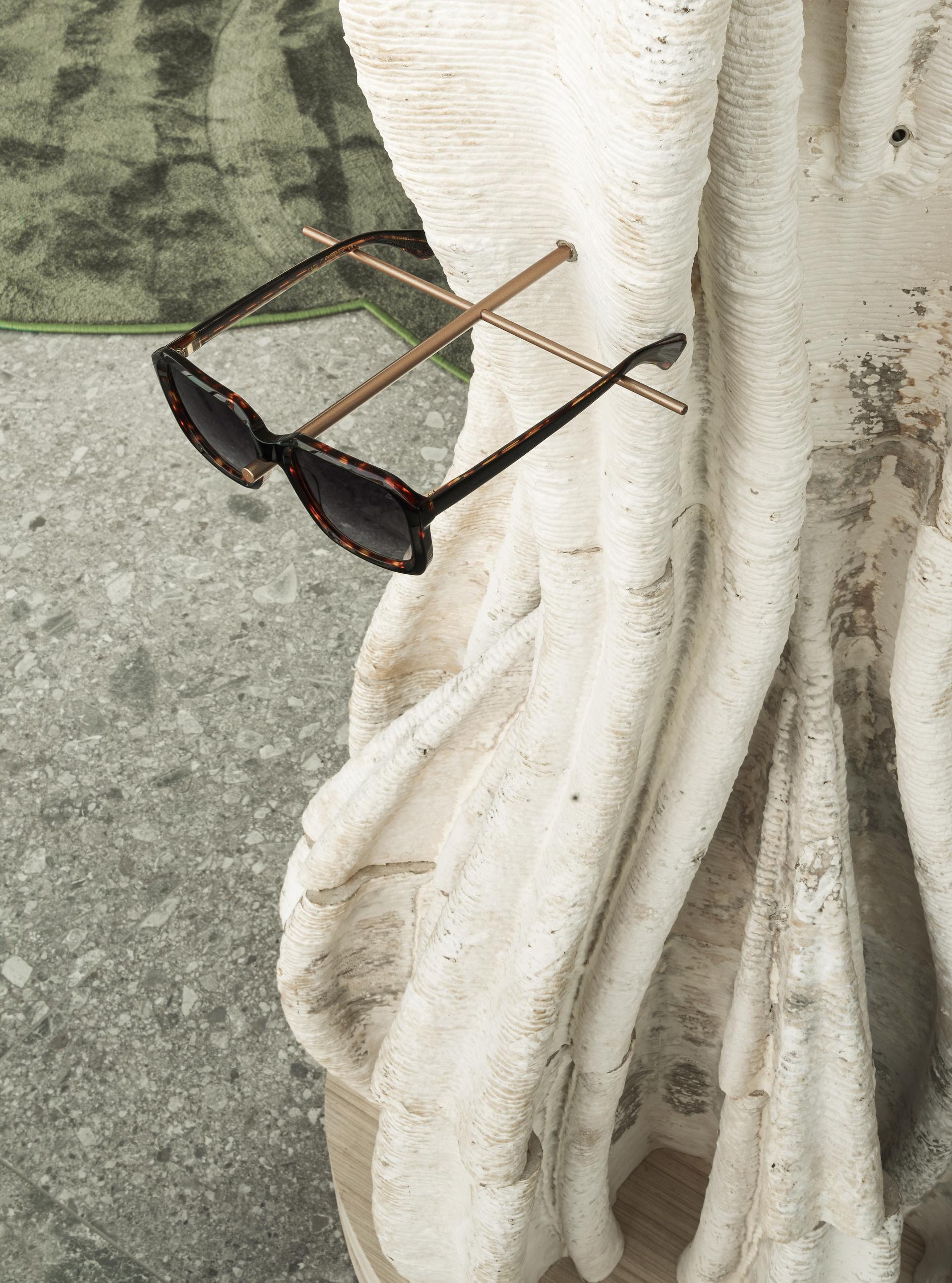 Sunglasses resting on a sculptural, tree-inspired stand made from natural materials, emphasizing eco-friendly design.