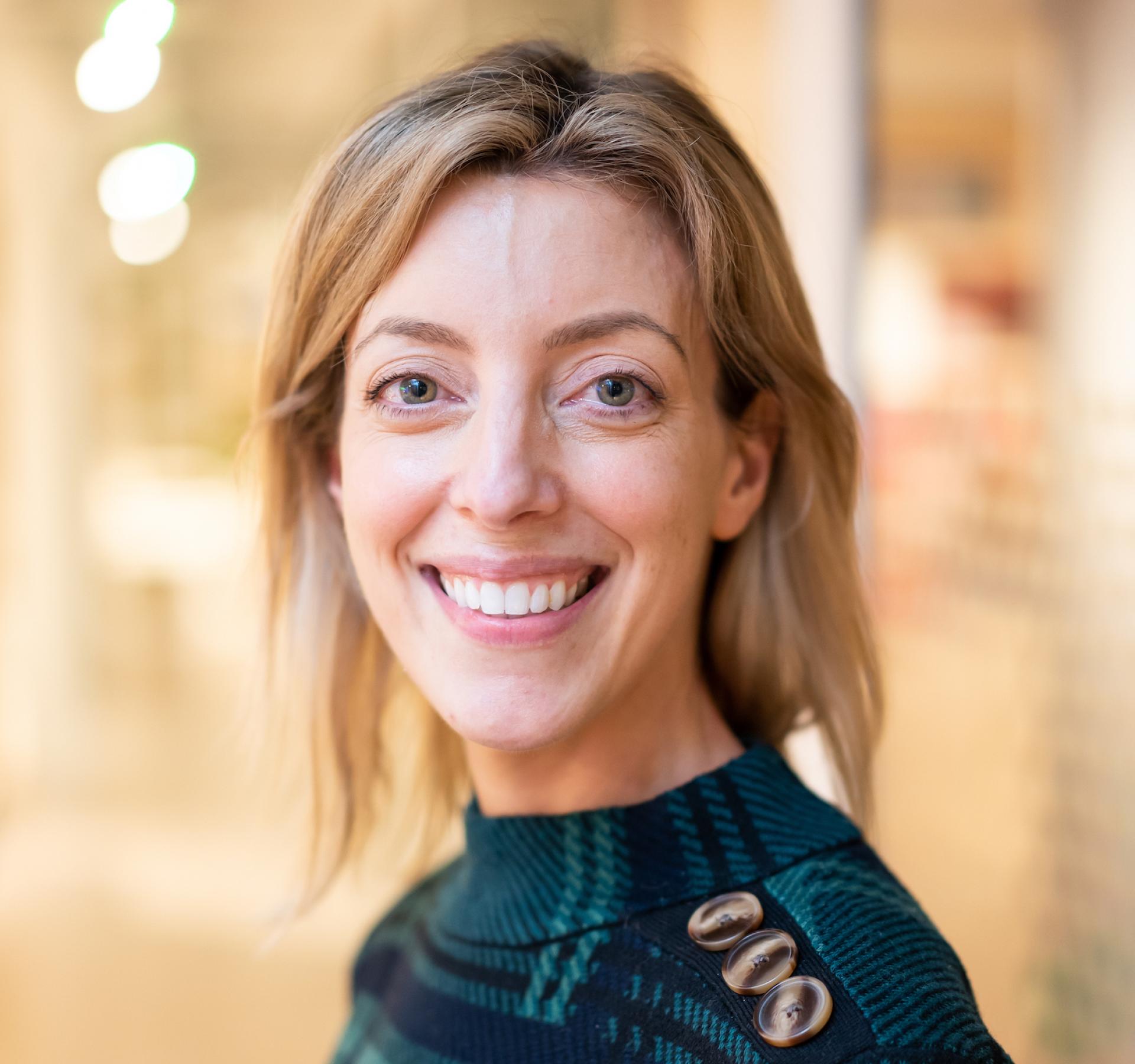 Smiling woman with light hair, wearing a green patterned sweater, reflecting optimism about the future of education.