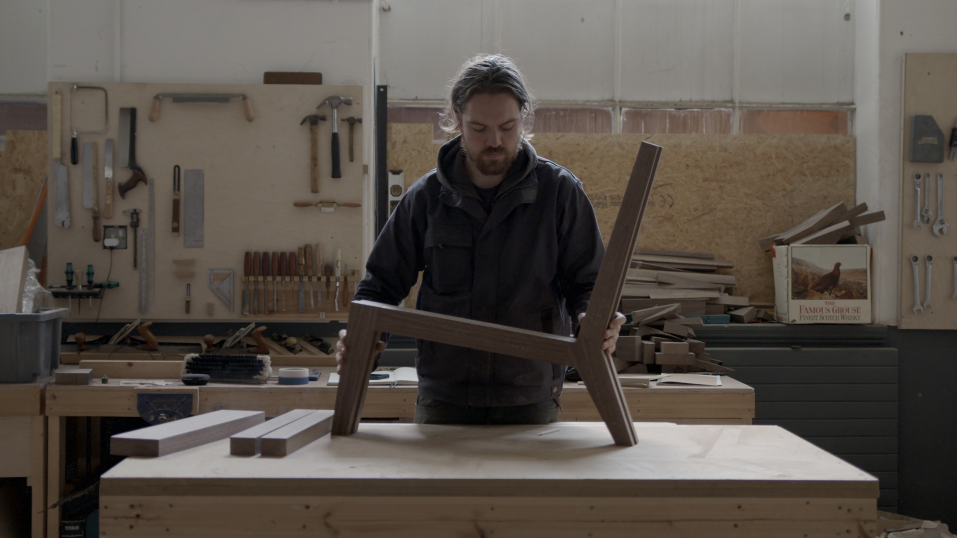 Craftsperson assembling a wooden chair in a workshop, surrounded by tools and materials, highlighting Glasgow's creative craft scene.