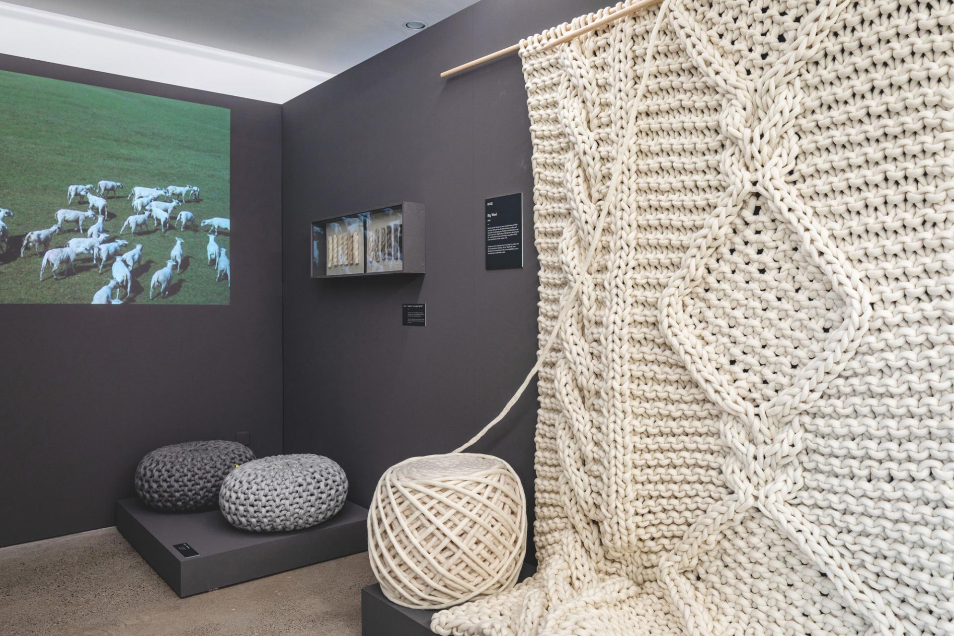 Exhibition display featuring Christien Meindertsma's textile art, including a knitted wall hanging and sculptural poufs.