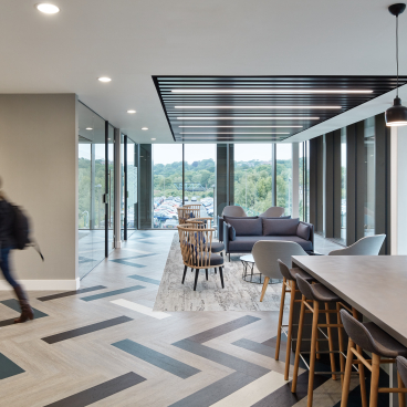 Modern office interior featuring open workspace, stylish seating, and large windows overlooking a green landscape, designed for healthcare professionals.