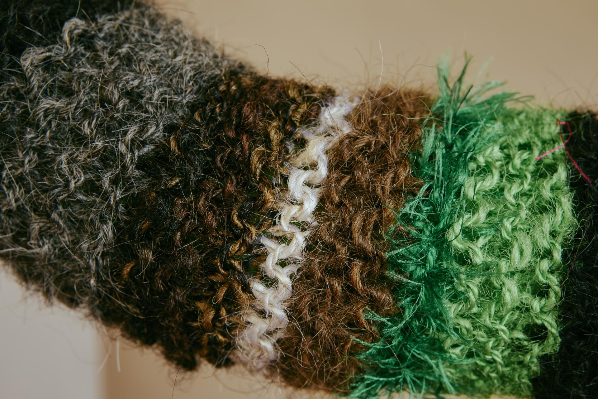 Textured fabric patch made of human hair in various earthy tones, exploring innovative material use in design.