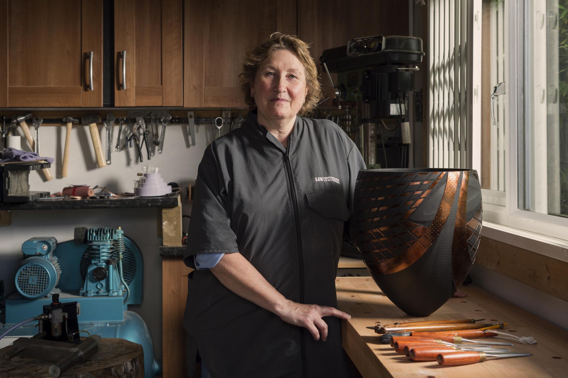 Craft artist in workshop showcasing intricate woodturning piece alongside various carving tools in north west England.