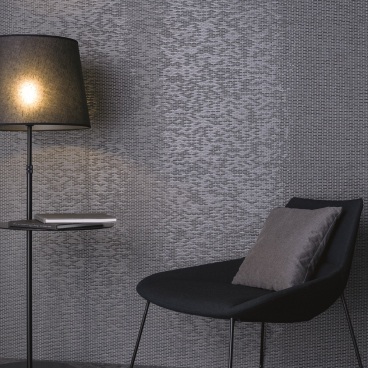 Elegant black chair with a pillow beside a lamp and textured gray wall, reflecting winter's earthy clay tones.