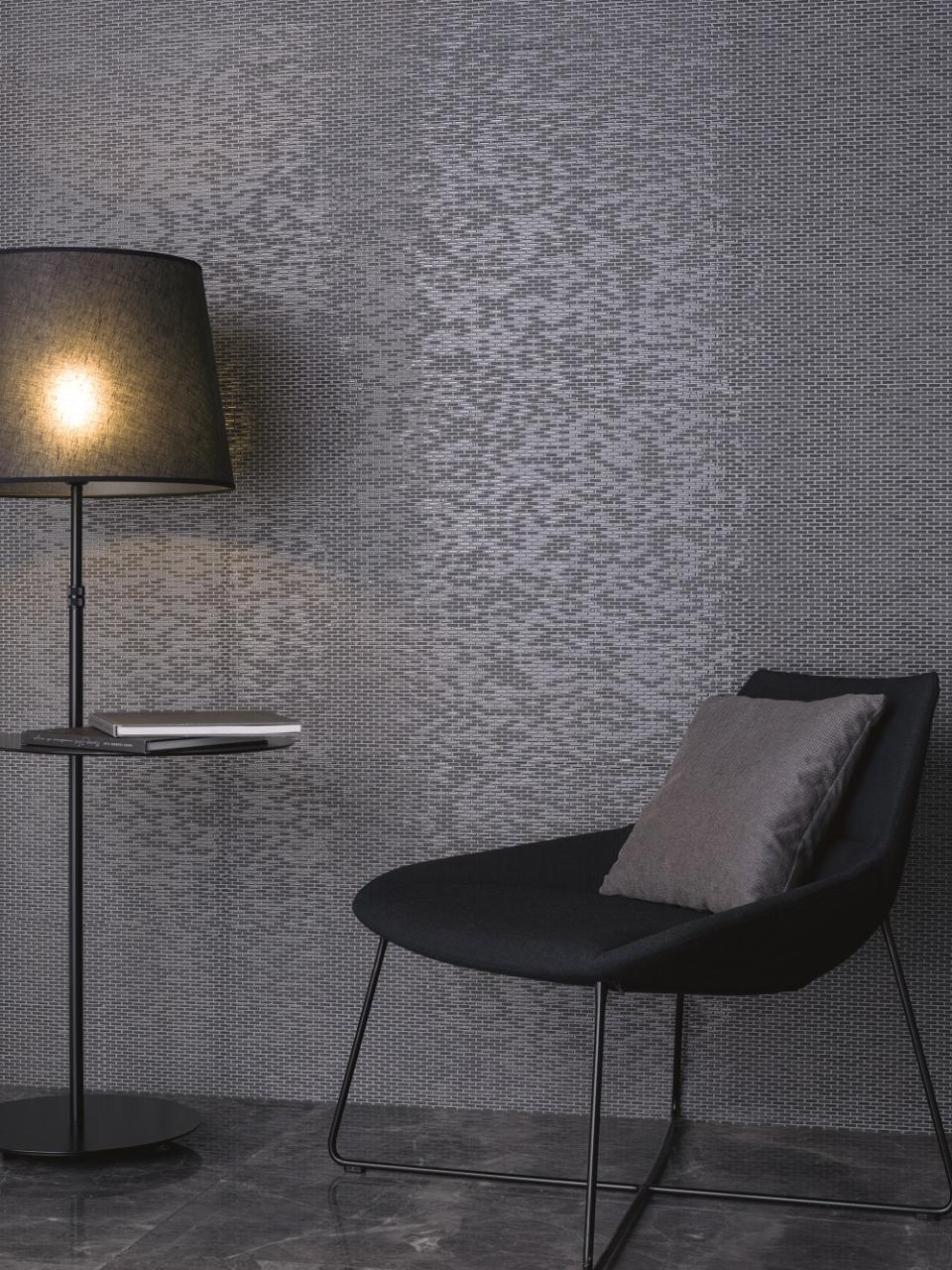 Elegant black chair with a pillow beside a lamp and textured gray wall, reflecting winter's earthy clay tones.