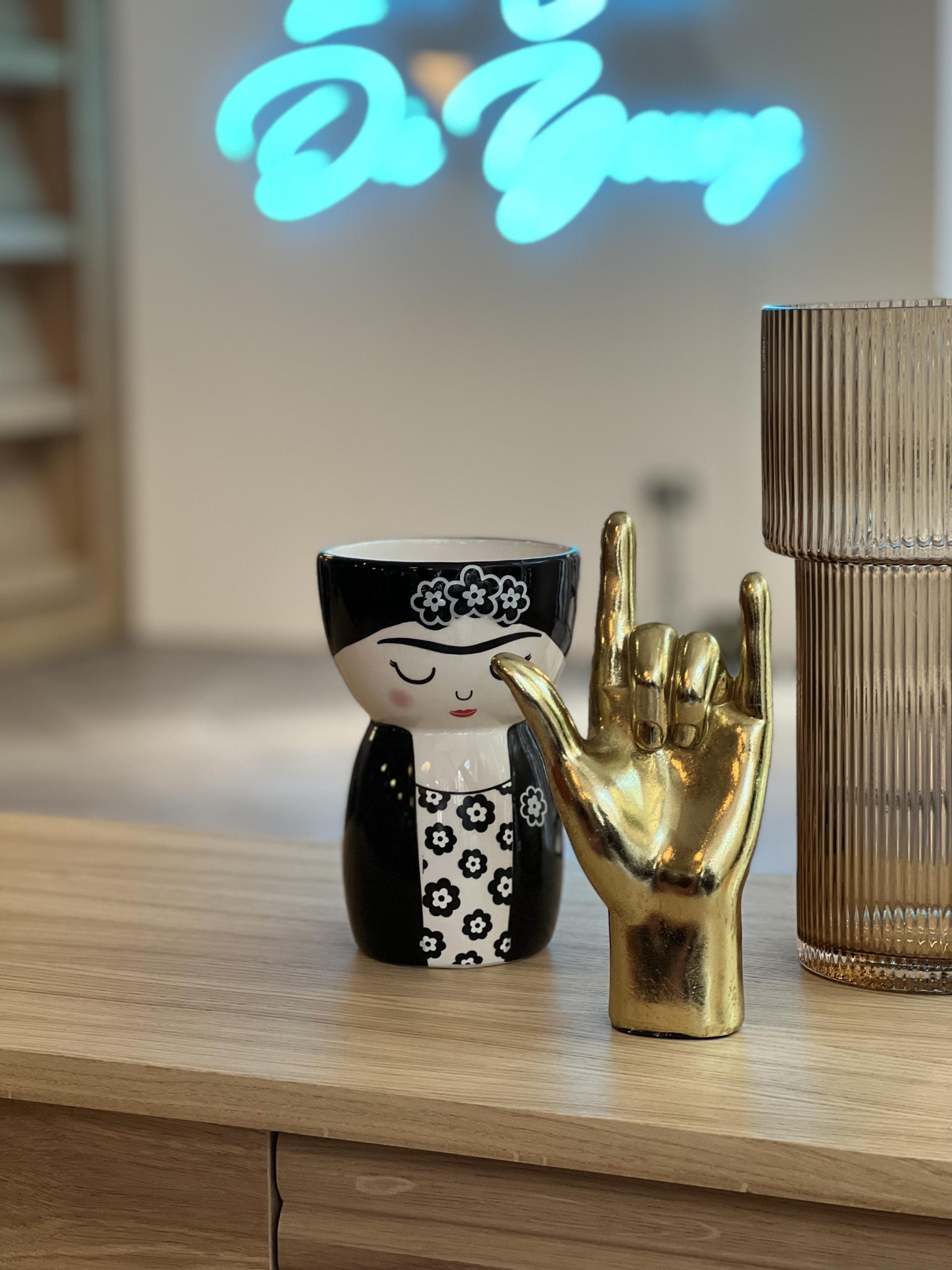 Vibrant decor featuring a ceramic doll, golden hand gesture, and textured vase in a stylish co-working space.